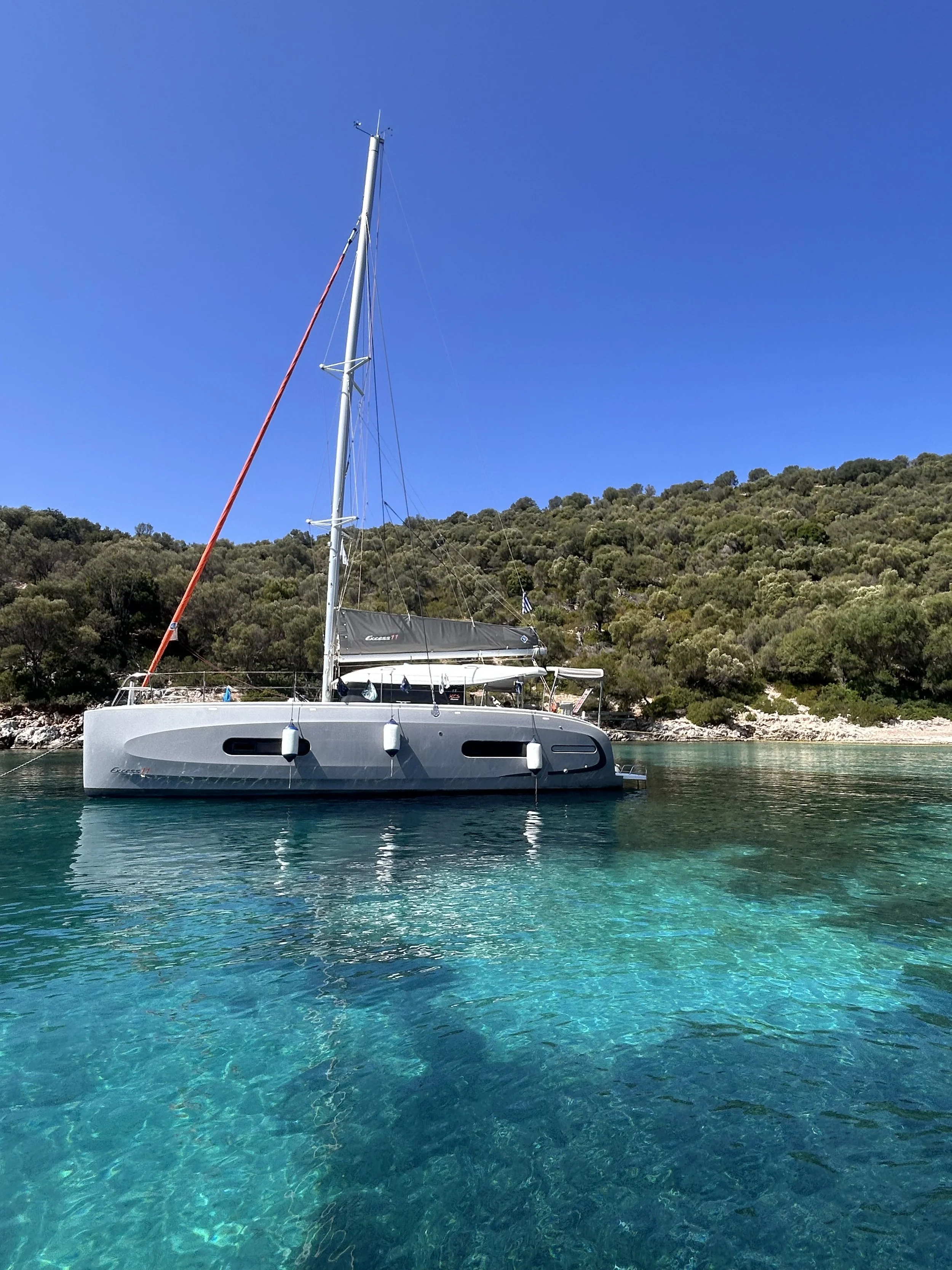 Nave a vela nel mare blu con una collina ricoperta di vegetazione sullo sfondo.