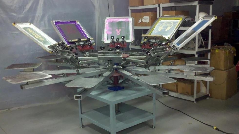 A screen printing machine with multiple color stations and screens set up in a workshop or print shop.