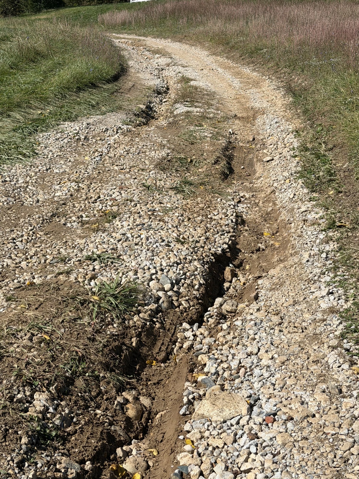 Washed-out gravel driveway with deep rain ruts needing repair in east central Indiana