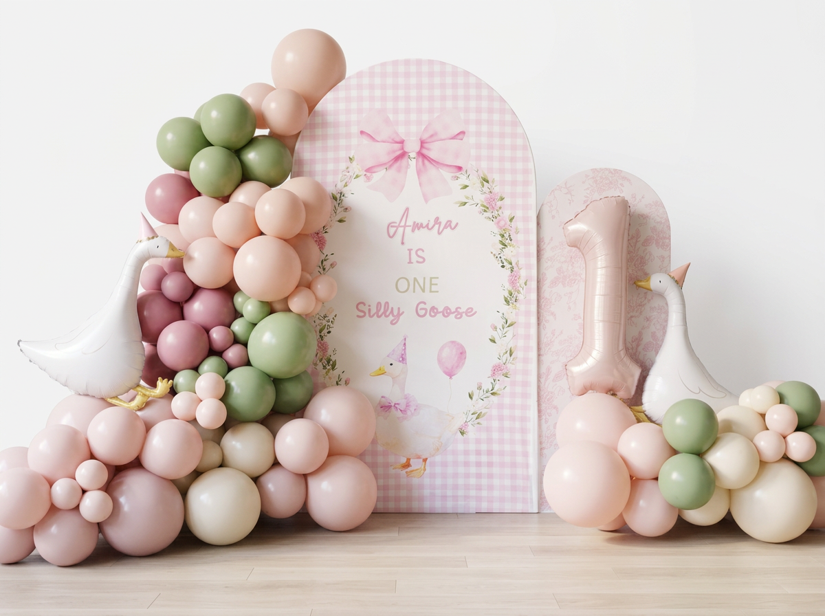 One silly goose themed arch backdrop with pastel colored green, blush pink, baby pink balloons adorned with goose foils and a soft metallic pink number one