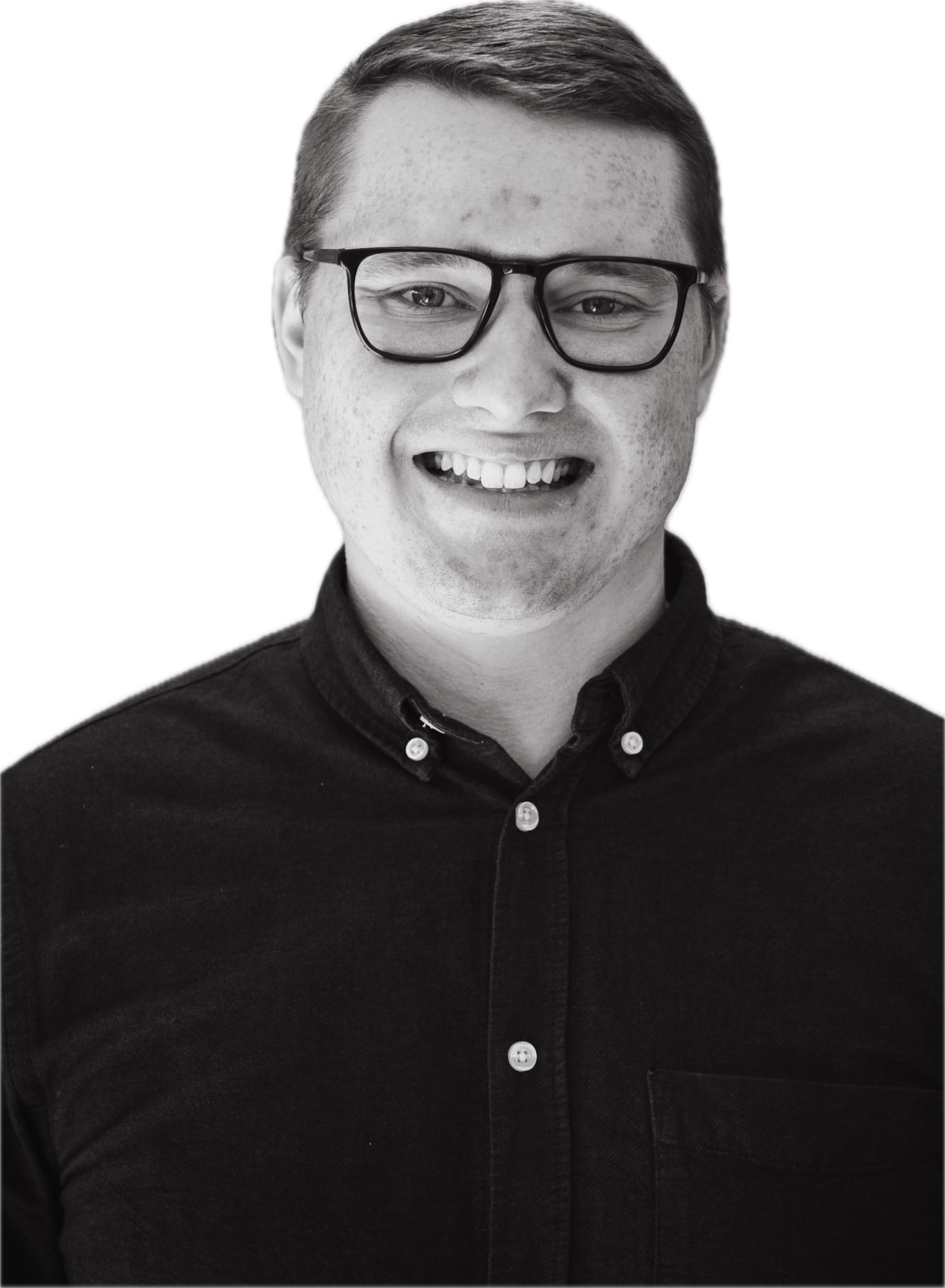 A young man with glasses smiling, wearing a button-up shirt, in black and white.