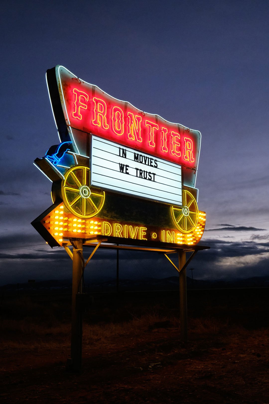 Vintage neon sign at the entrance of the Frontier Drive-Inn, stating "in Movies We Trust".