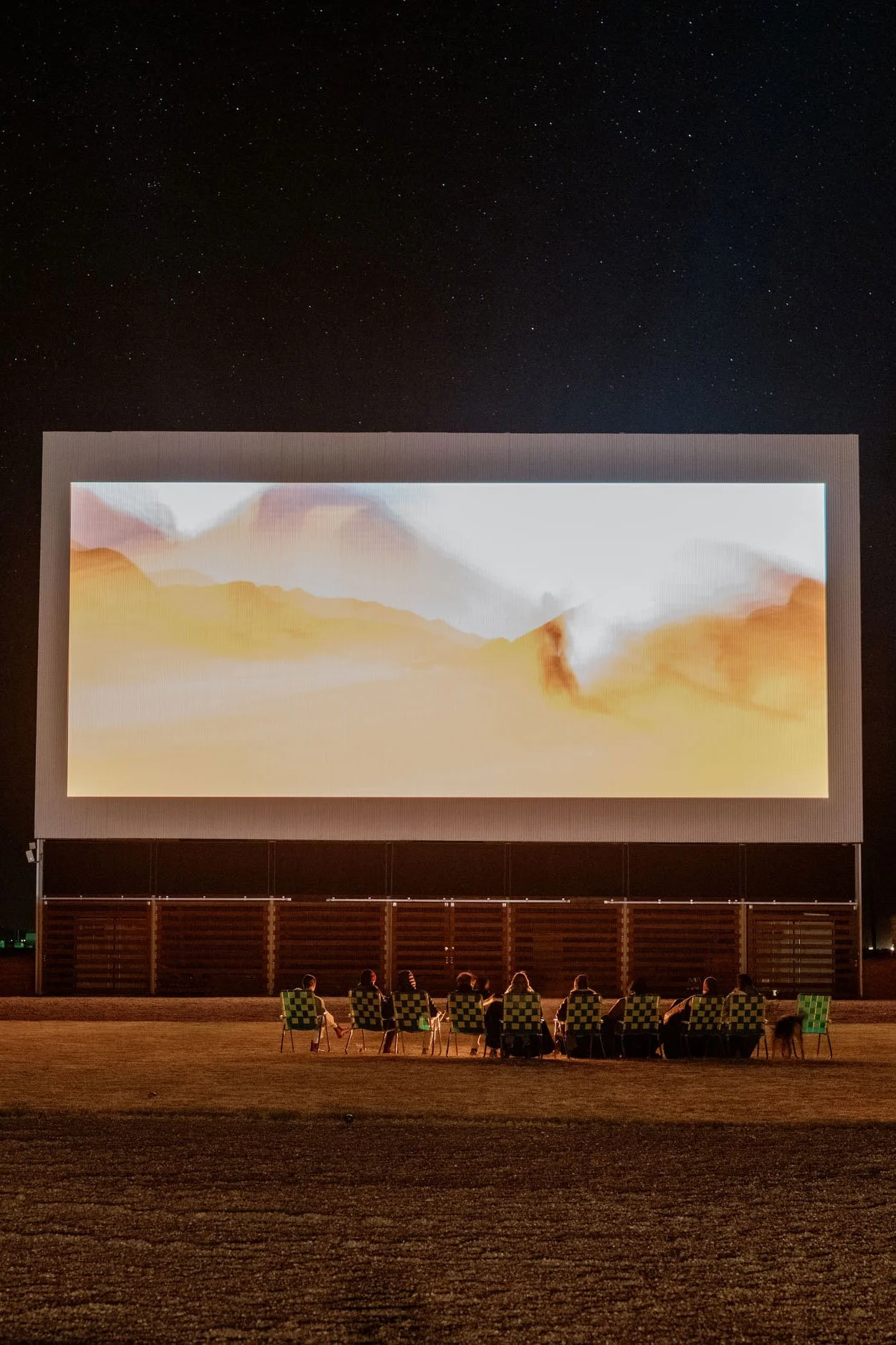 A group in green and white lawn chairs gathers in front of the big screen at the Frontier Drive-Inn