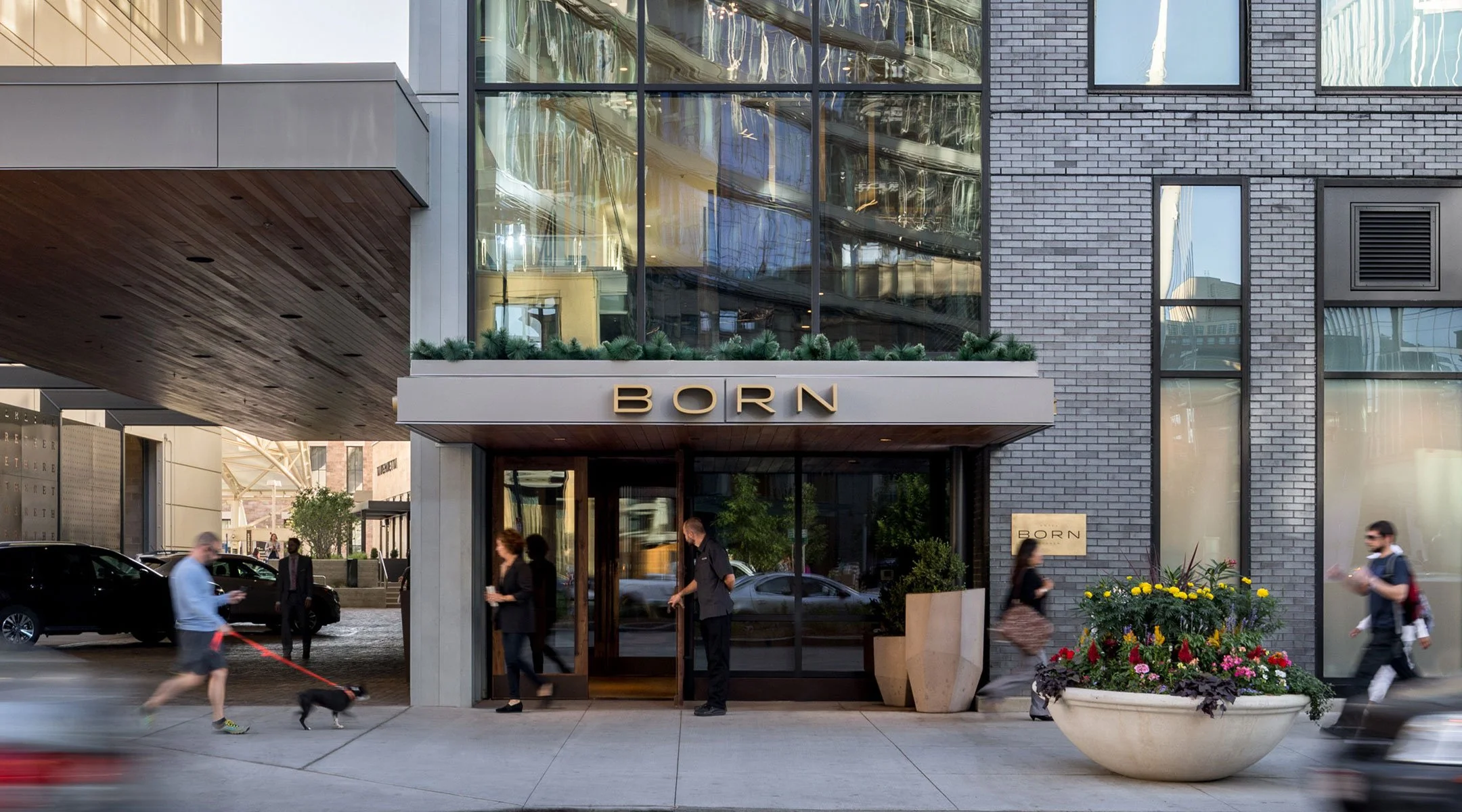 A woman exits the main entrance of the Born Hotel while a man holds the door for her.