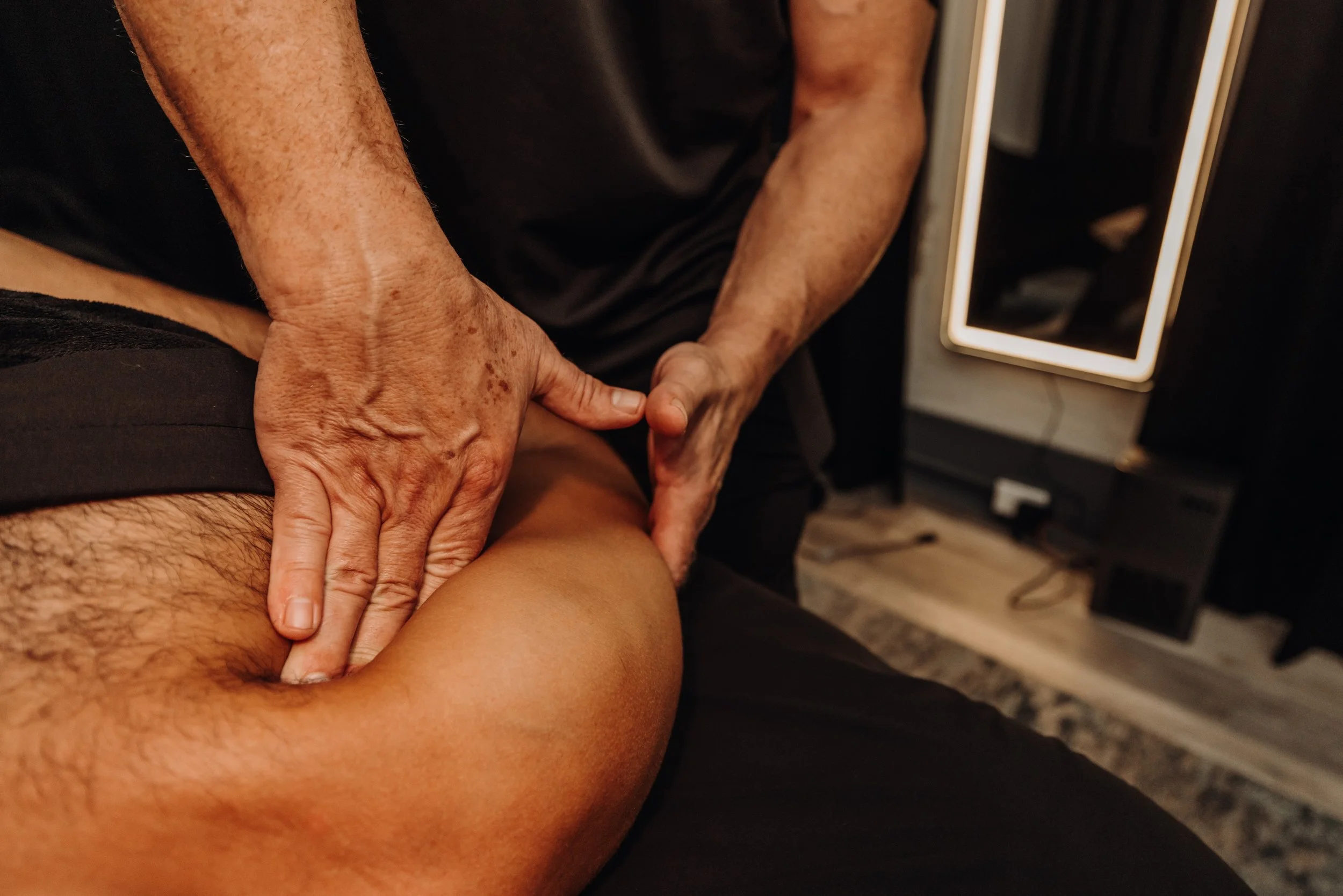 A person receiving a massage or physical therapy on their thigh, with another person applying pressure with their hands.
