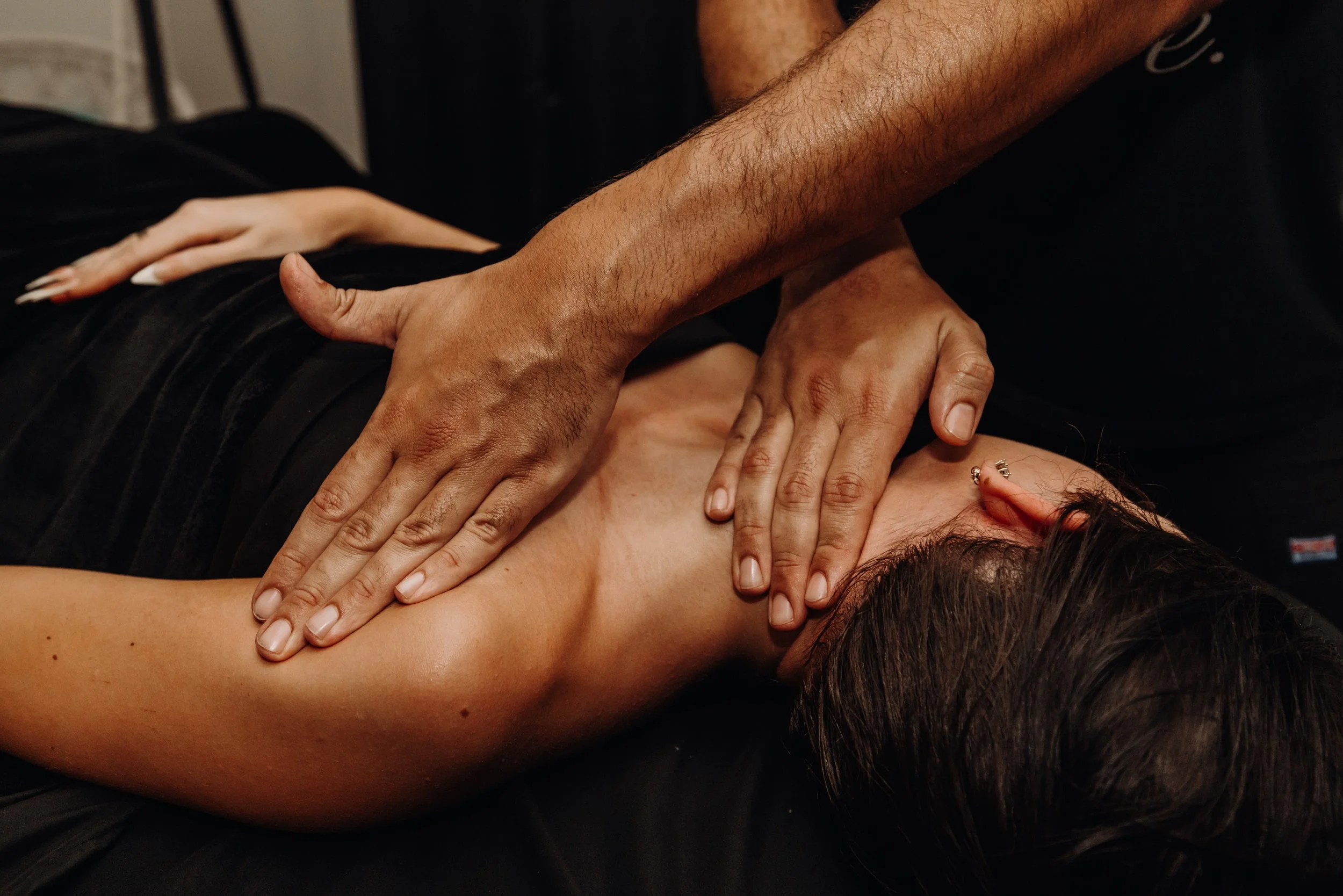 A person receiving a massage from another individual, with one hand on the person's lower back and the other hand on their upper back.