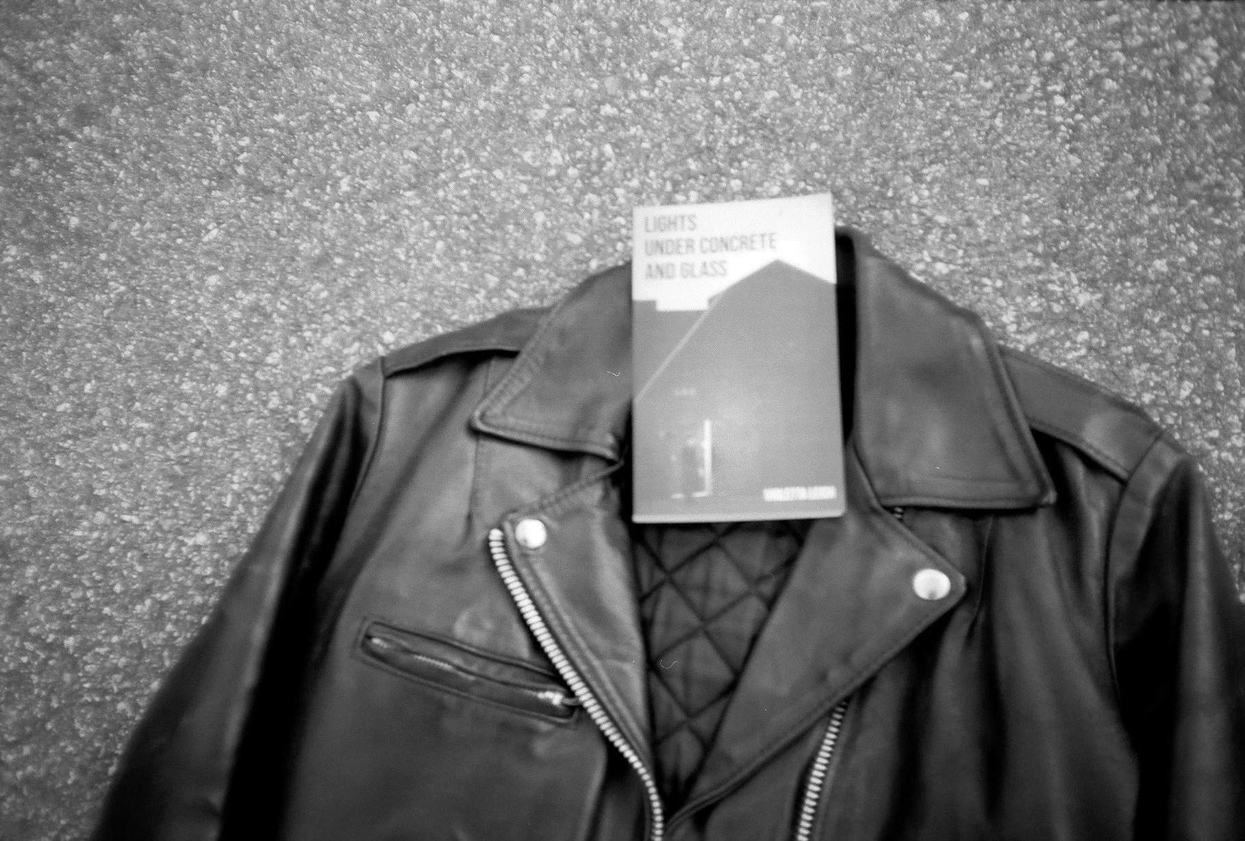 The Violetta Leigh book of prose poetry, Lights Under Concrete and Glass, sits in the open lapels of a leather jacket.
