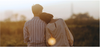 A couple walking together outdoors at sunset, with one person resting their head on the other's shoulder.