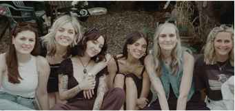 Six young women sitting outdoors on a bench, smiling at the camera.