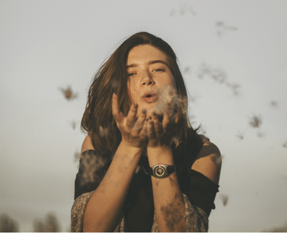 Young woman blowing dandelions outdoors on a cloudy day