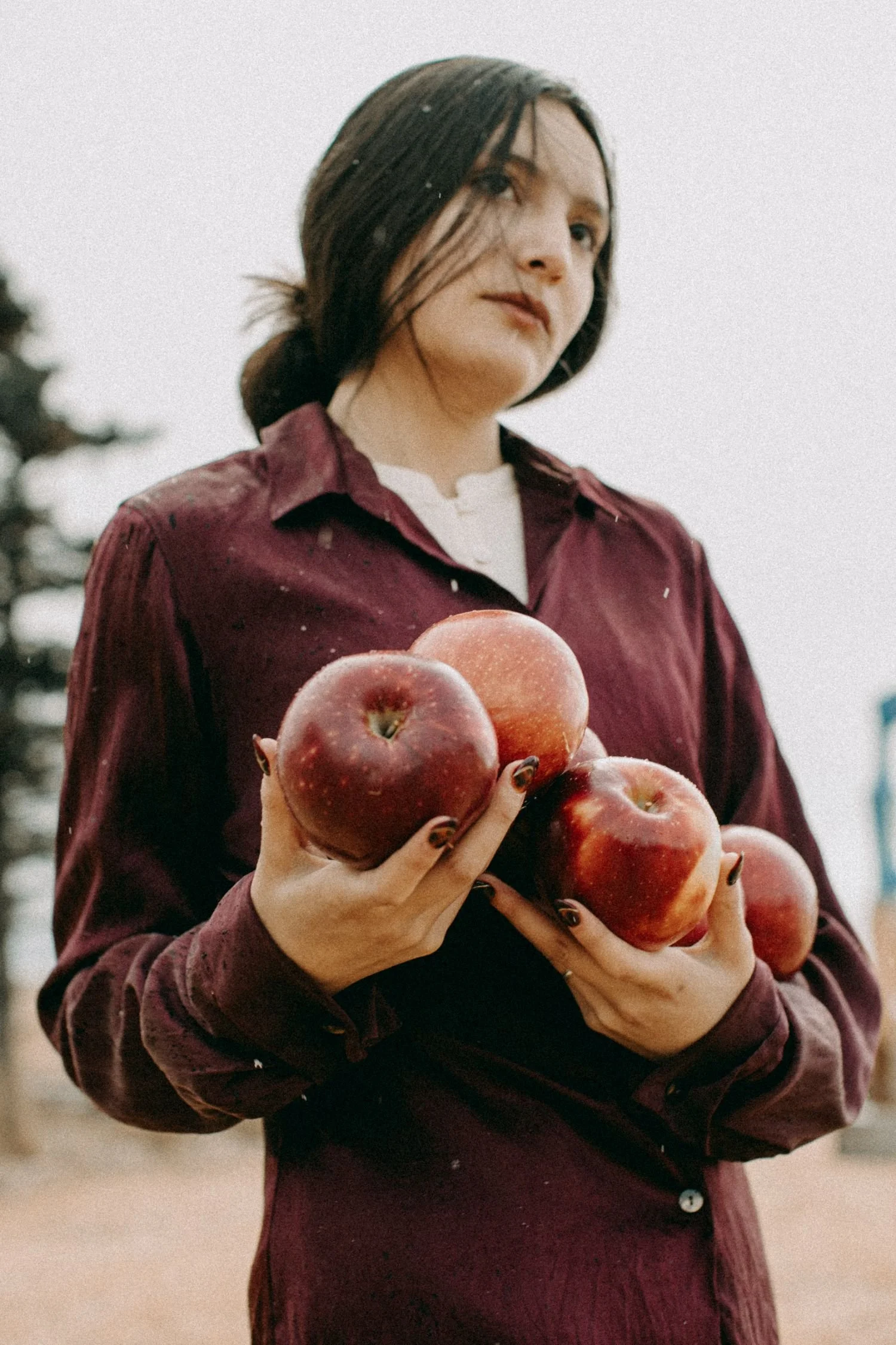 A woman with dark hair wearing a maroon jacket holding several red apples.