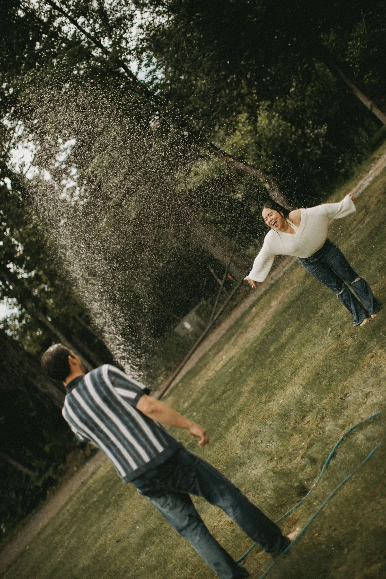 A woman laughing and playing in a yard during a water spray, with two men nearby.