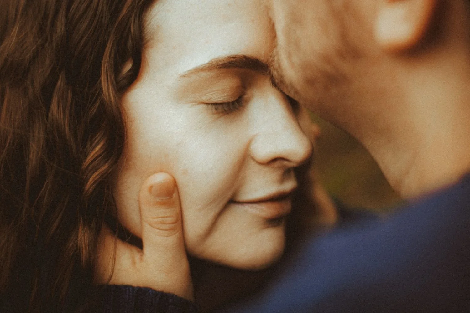 A couple sharing an intimate moment, gently touching foreheads with closed eyes and serene expressions.