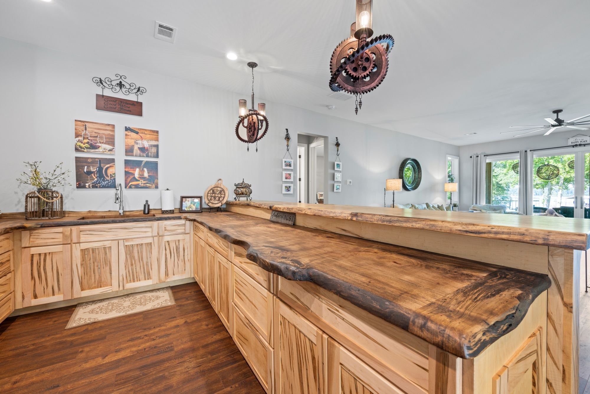View of a home's open-concept living area with a rustic kitchen counter made of live-edge wood, modern decor, artwork on the wall, and large windows with outside greenery.