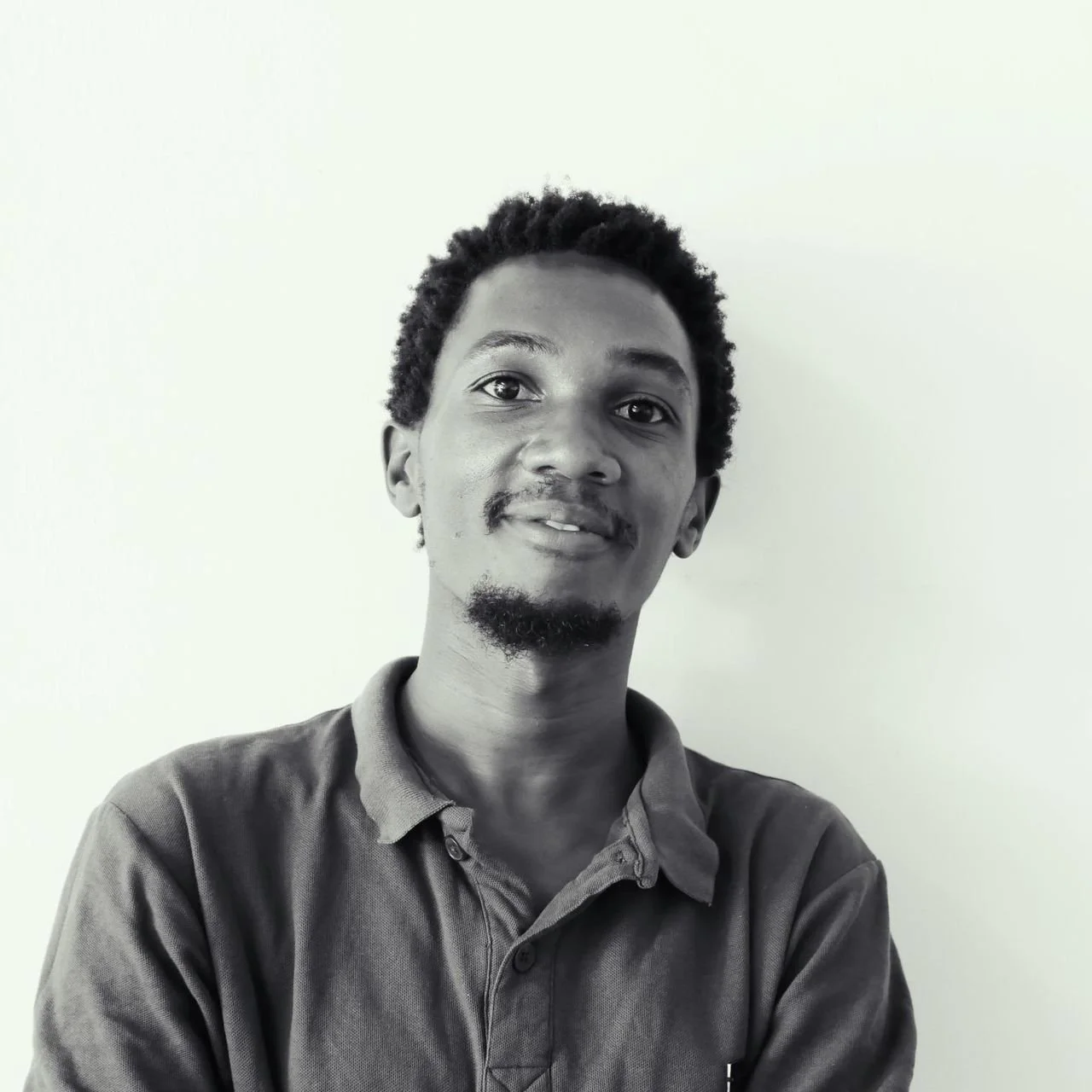 Black and white portrait of a young man with short curly hair and facial hair, wearing a collared shirt, smiling slightly, against a plain light background.