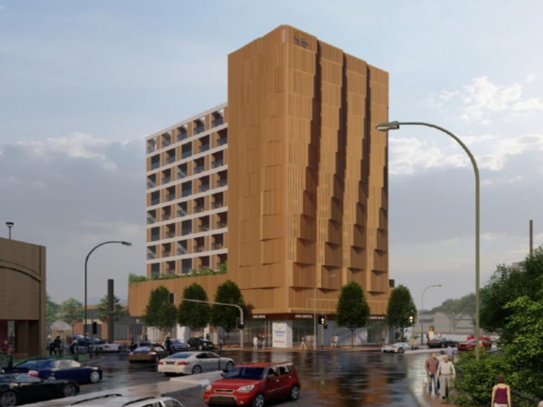 A multi-story building with a modern design, featuring a brown exterior with vertical patterns, a rooftop garden, and ground-level retail space. The street includes cars, trees, and pedestrians.