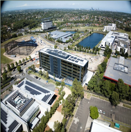 Aerial view of a modern urban area with office buildings, a sports field, a pond, and parking lots.