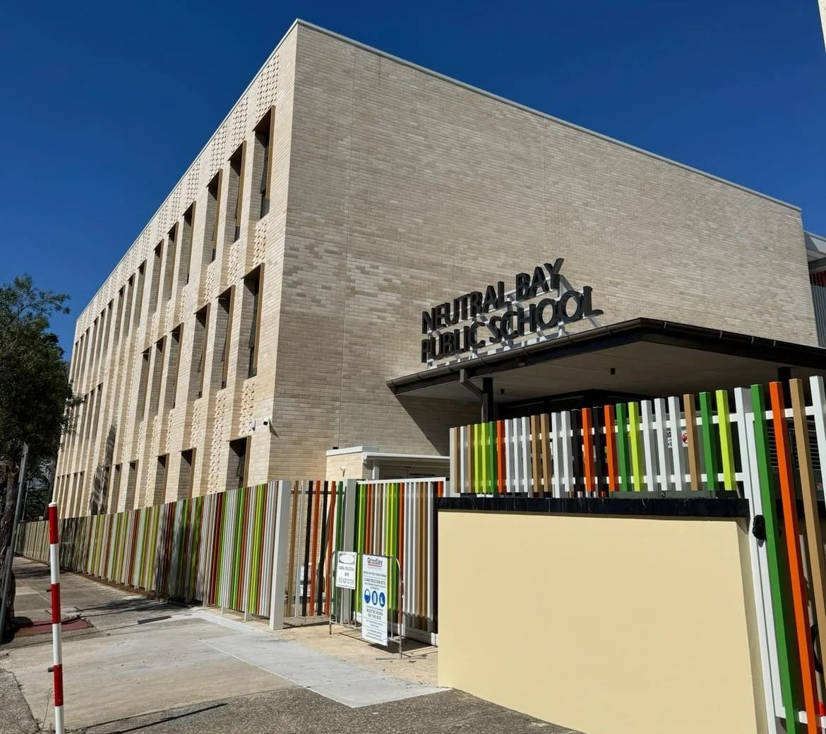 Exterior of Neutral Bay Public School building with colorful fence, blue sky, and school sign.