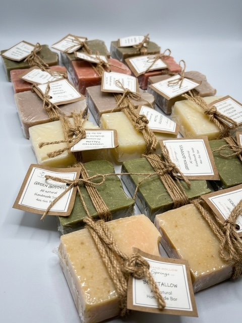 Assorted handmade soap bars wrapped with twine and tags, displayed on a white surface.