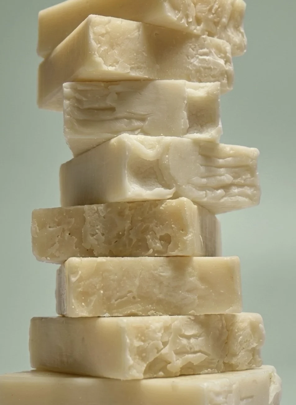 Stack of various white and cream-colored soap bars with textured surfaces, arranged vertically against a light background.