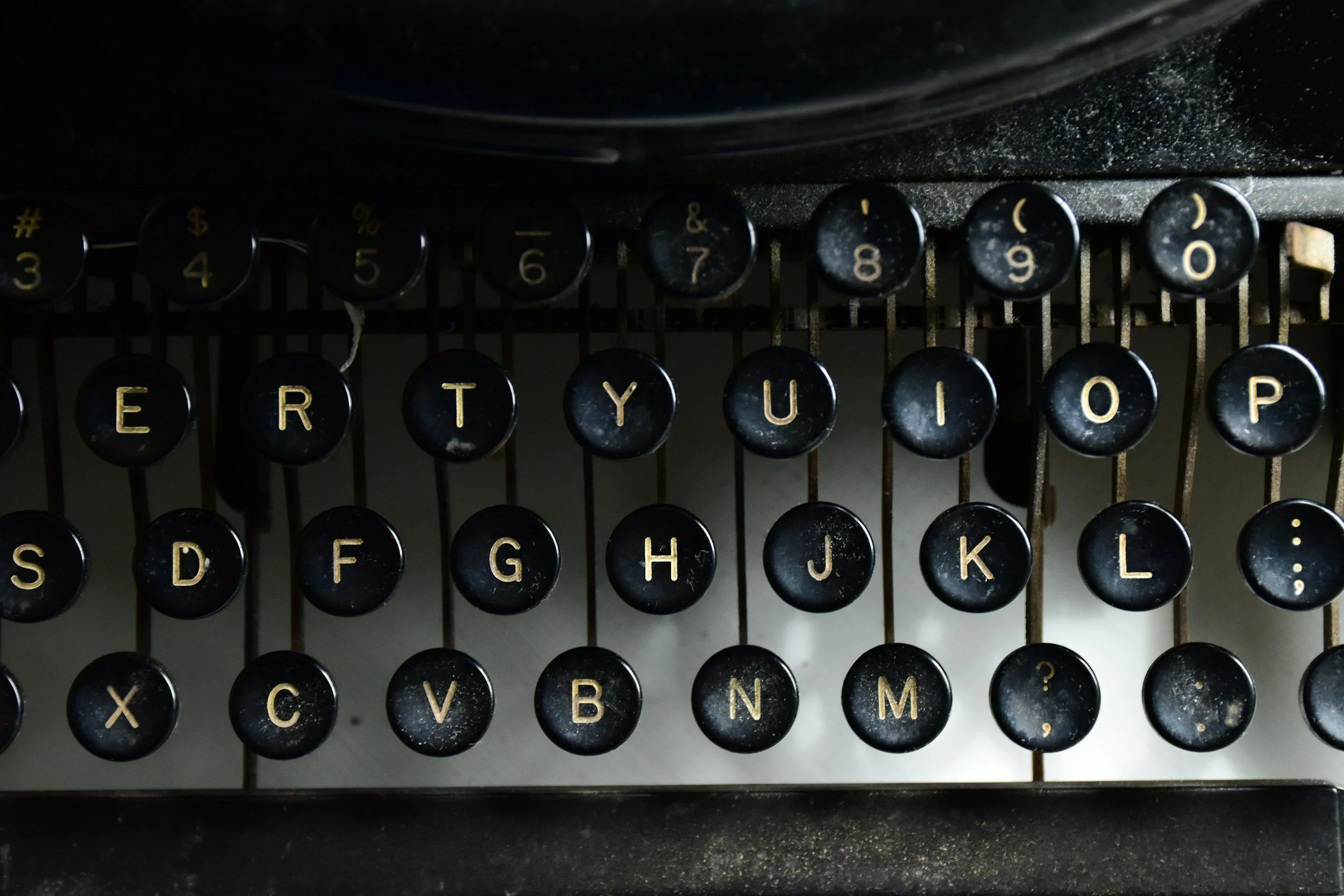 Close-up of an old typewriter keyboard with black keys and yellow lettering, showing some dust and signs of age.
