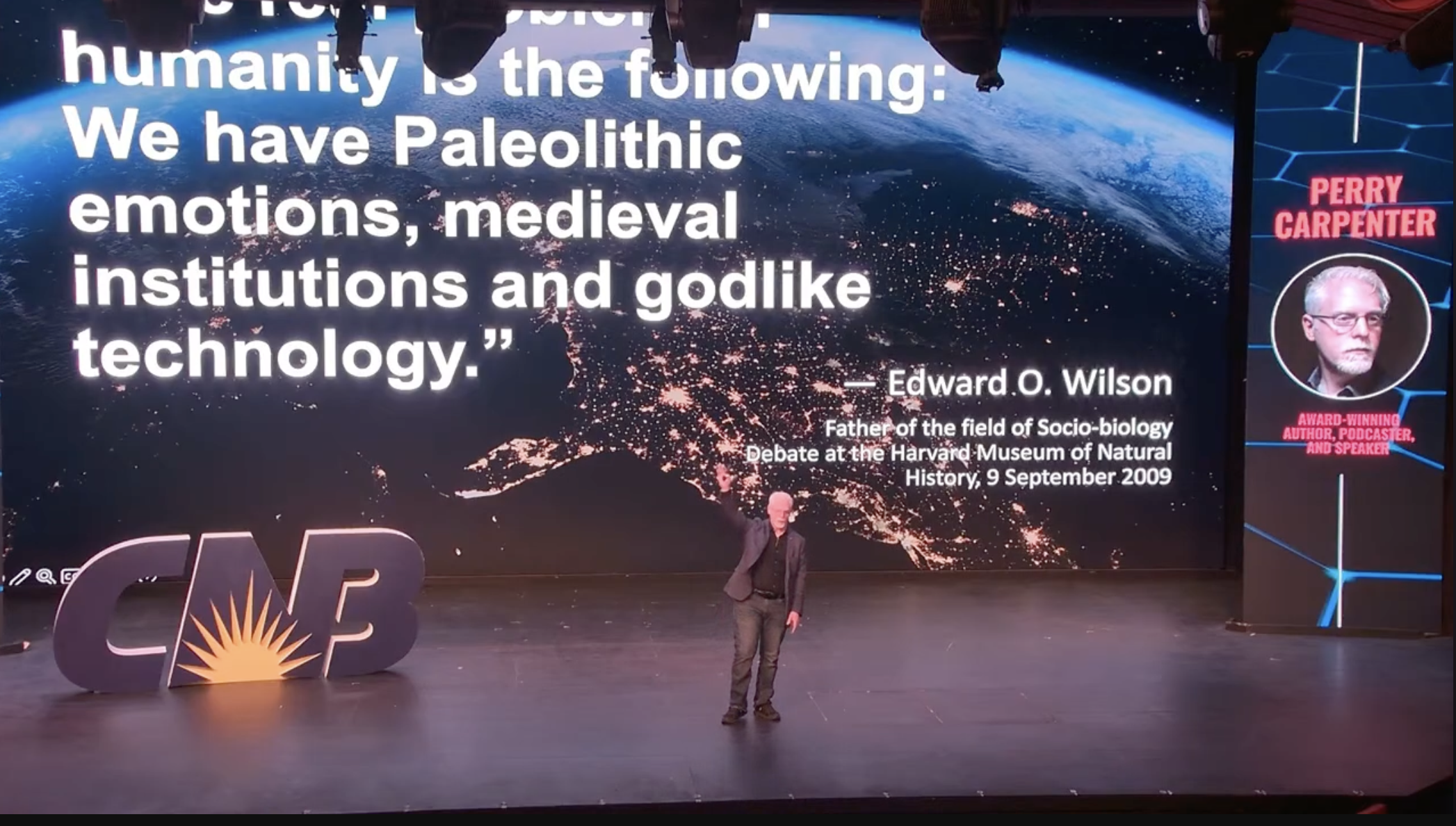 Perry Carpenter presenting on-stage with a large quote about humanity behind him.