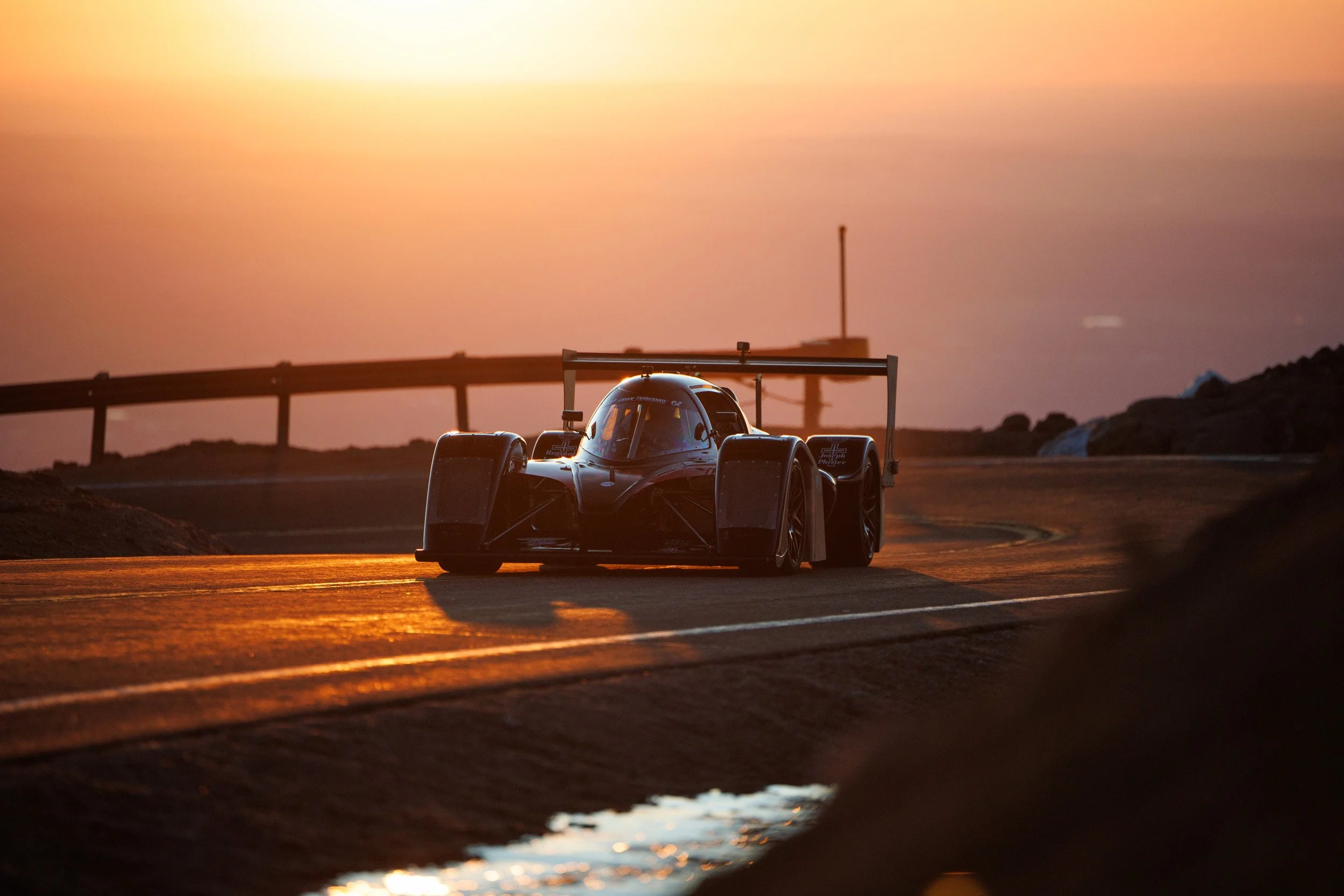 A race car on a track during sunset, with the sky in hues of orange and pink.