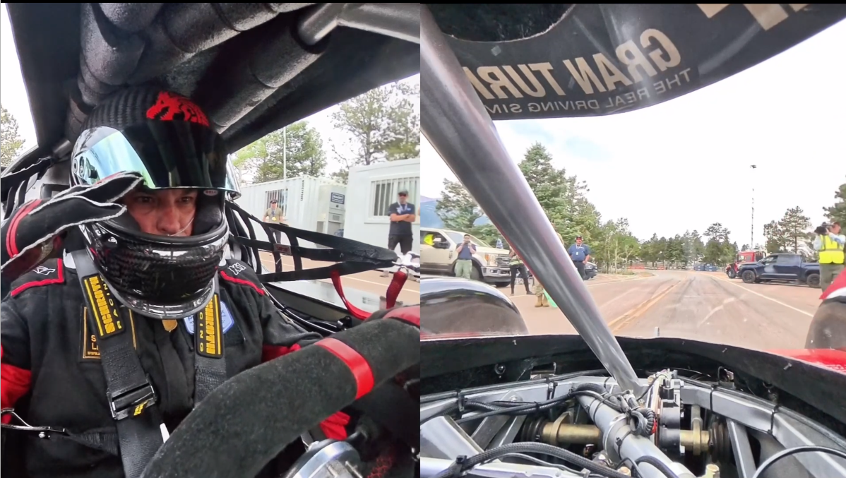Driver in racing suit and helmet inside race car, with a view of the road and officials outside during a race.