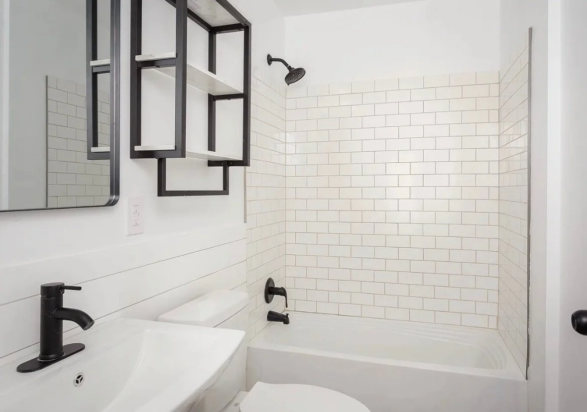 Modern bathroom with white subway tile on walls, black fixtures, a bathtub, a sink, and a decorative black metal wall shelf.