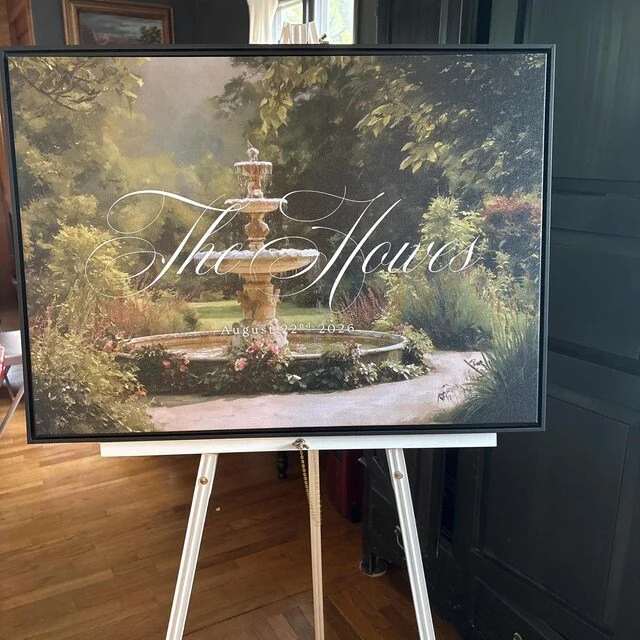 Wedding welcome sign featuring a painted garden fountain background that reads "The Hours" and the date "August 22nd, 2026". Handmade by January Swift Studio.
