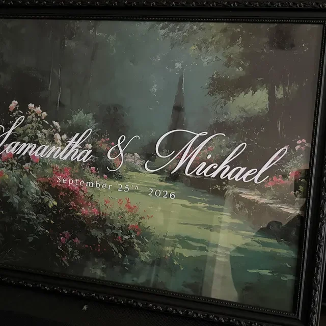 A framed wedding sign featuring a painted landscape with trees, green grass, and pink and red flowers, with the names Samantha and Michael and the date September 25th, 2026 in elegant script. Handmade by January Swift Studio.
