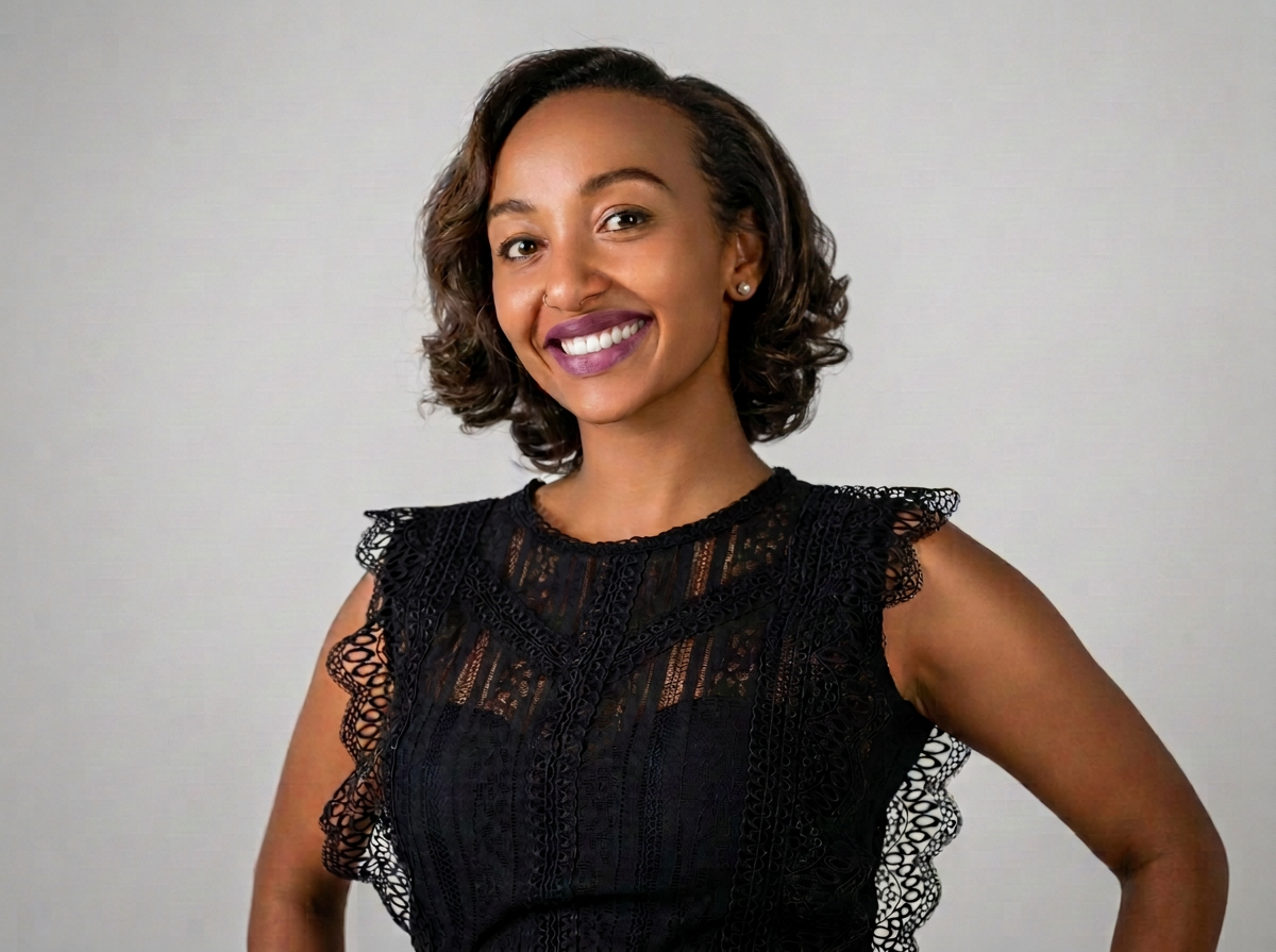 Smiling woman with curly hair wearing a black lace dress against a plain background.