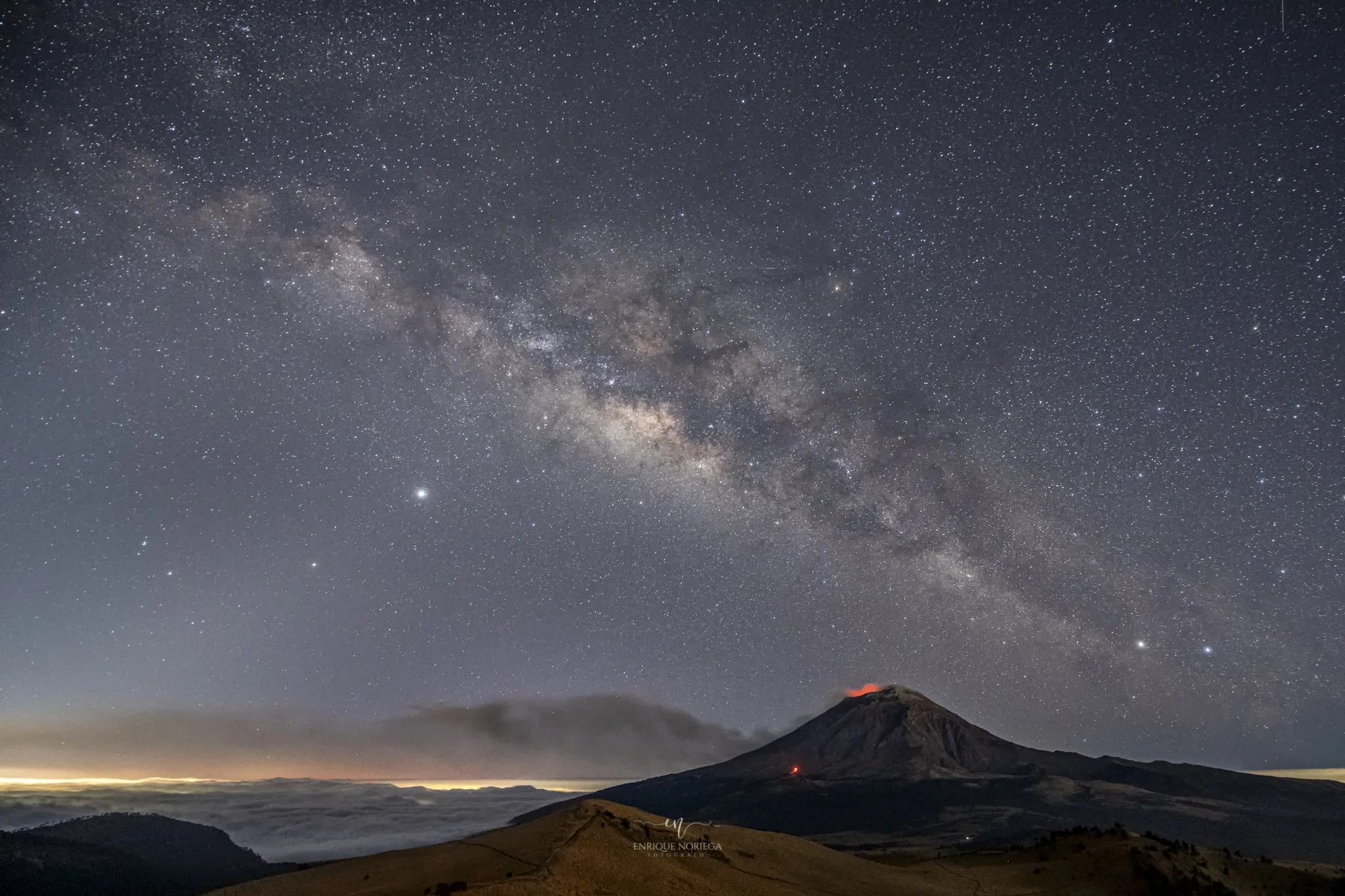 Vista de noche del cielo estrellado y la vía láctea sobre un volcán con cumbres y pendientes en primer plano