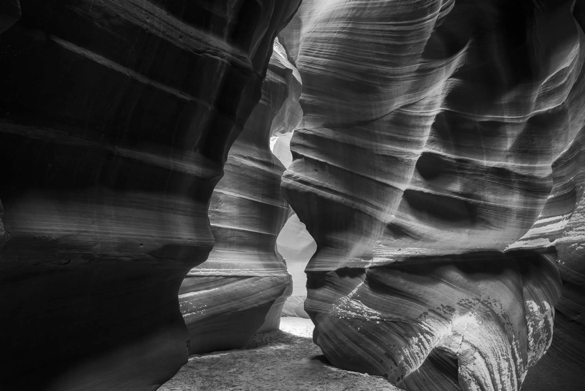 Foto en blanco y negro de un cañón o formación rocosa con paredes de capas estratificadas y curvas.