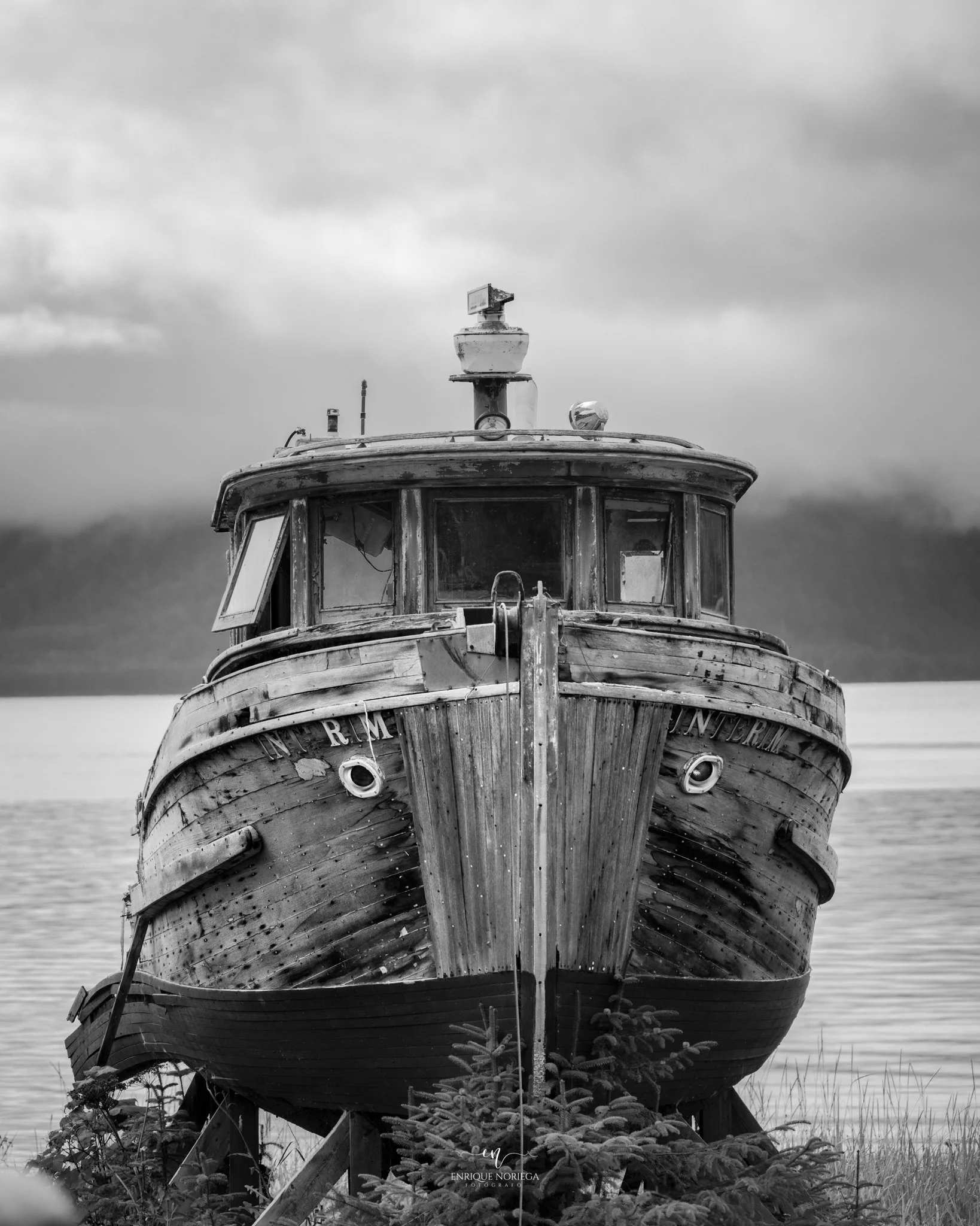 Barco viejo de madera en tierra, con cielo nublado al fondo.