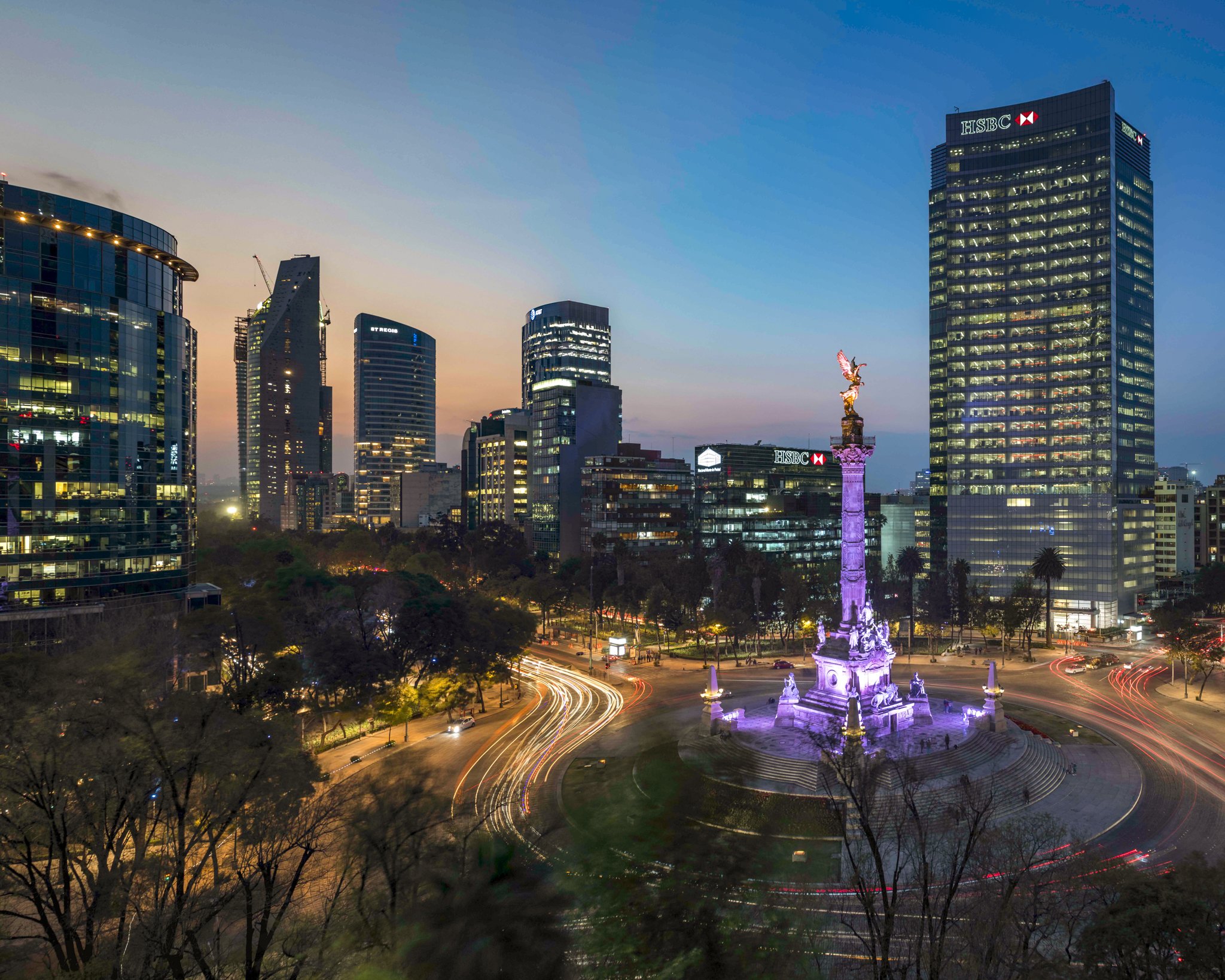 Vista del centro de la ciudad de la Ciudad de México durante el atardecer con rascacielos iluminados y la fuente de la Diana Cazadora iluminada en primer plano.