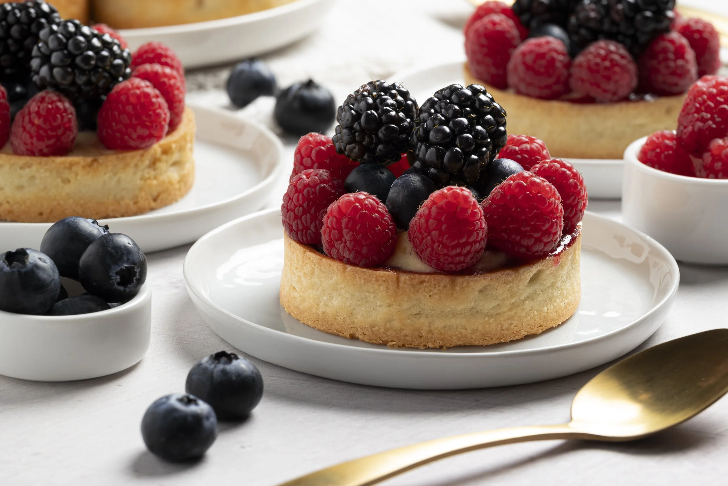 Tarta de vainilla decorada con frambuesas, moras y arándanos, servida en platos blancos, con frambuesas adicionales y moras alrededor.