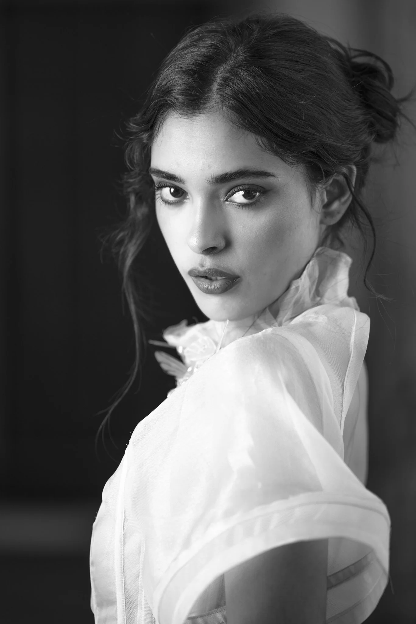 Retrato en blanco y negro de una joven con cabello rizado, expresión facial serena y mirada directa a la cámara, vestida con blusa ligera