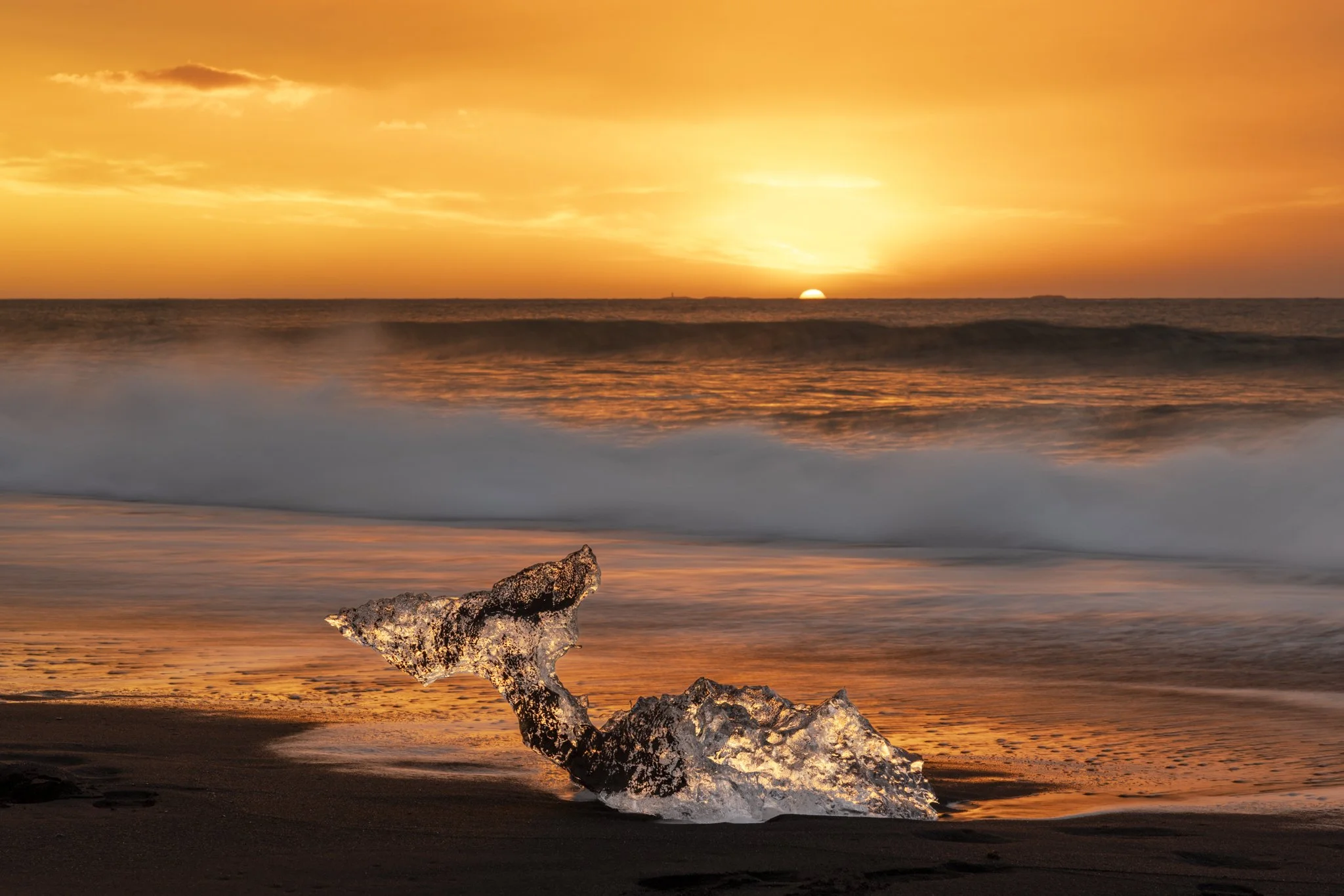Atardecer en la playa con un trozo de coral en primer plano y el sol poniéndose en el horizonte, reflejándose en el mar.
