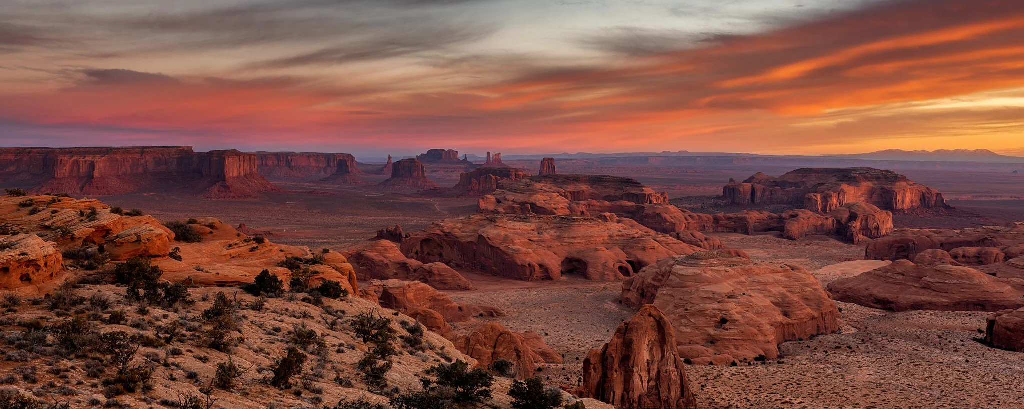 Paisaje del desierto con formaciones rocosas y montañas al atardecer, cielo con nubes y tonos anaranjados y rosados