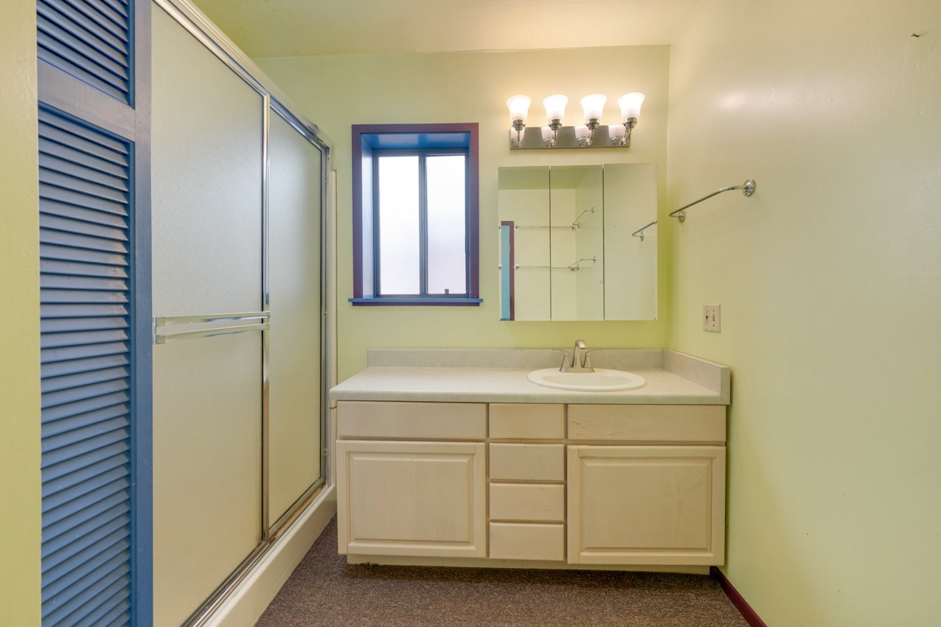 Bathroom with a sink, mirror, vanity with cabinet drawers, window, and a shower with sliding doors.