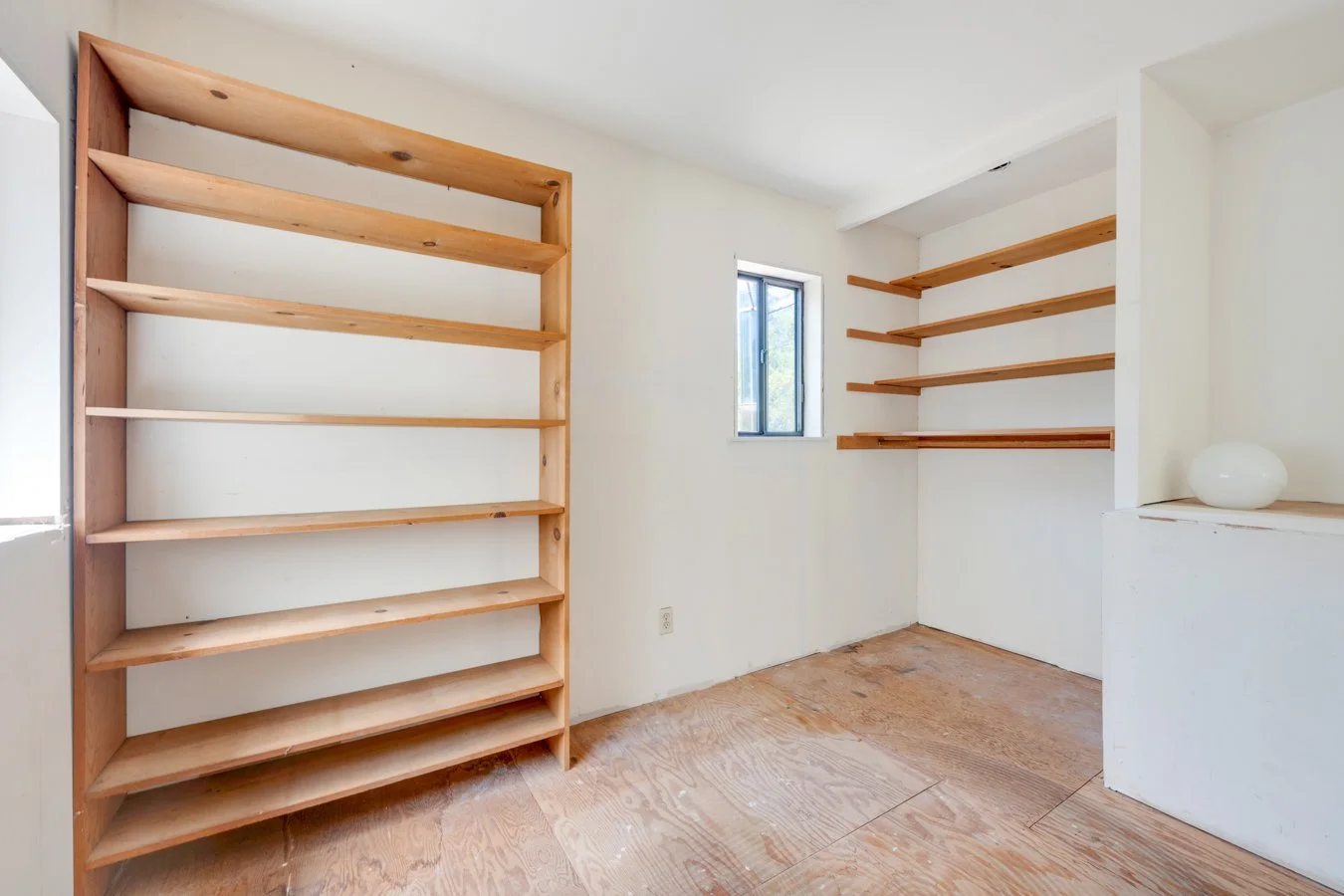 Empty room with wooden shelves on white walls and a small window.