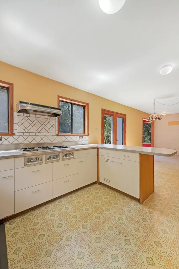 Kitchen with cream-colored cabinets, a gas stove, and two windows in a mustard yellow wall.