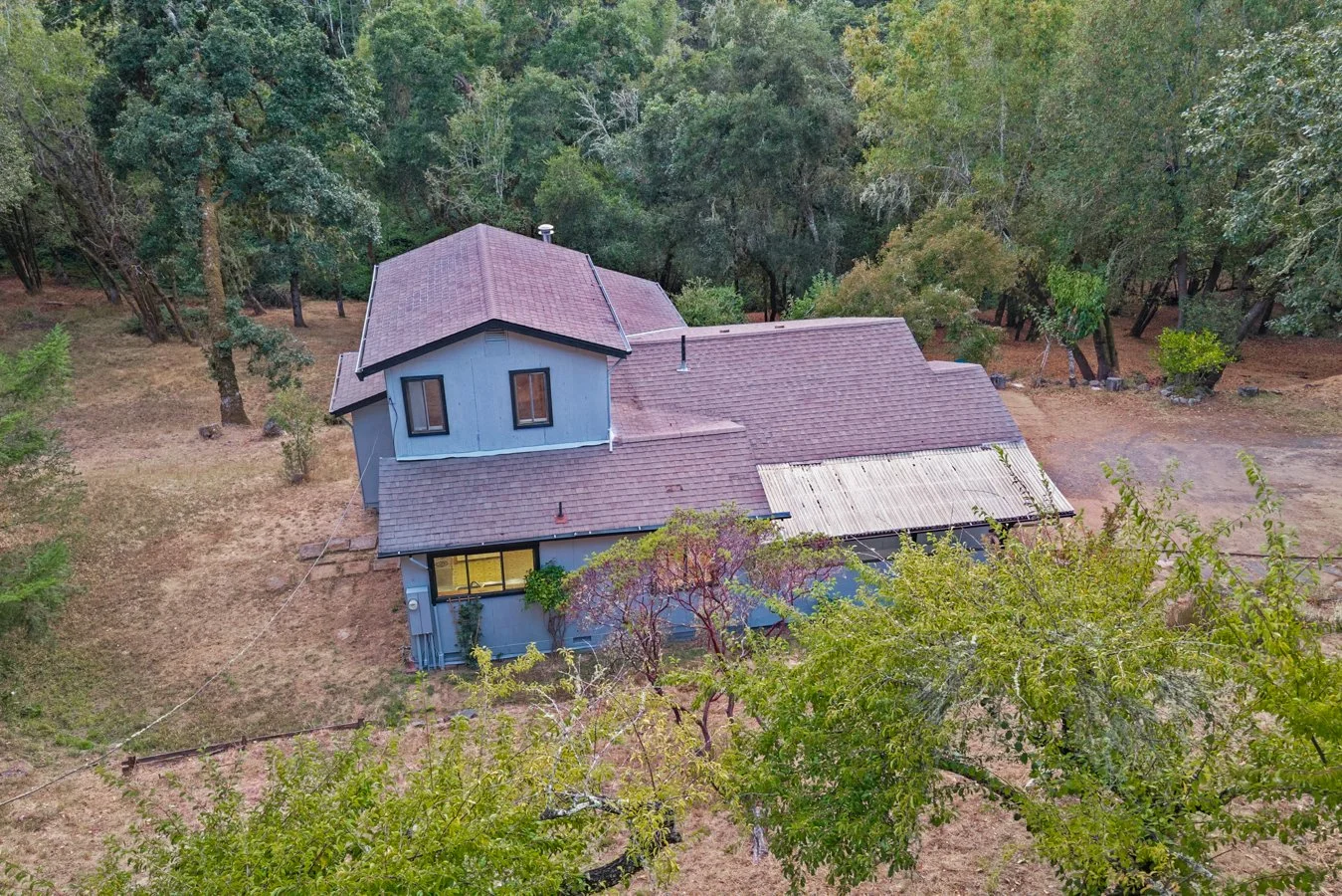 An aerial view of a blue house with a brown roof, surrounded by trees in a wooded area.