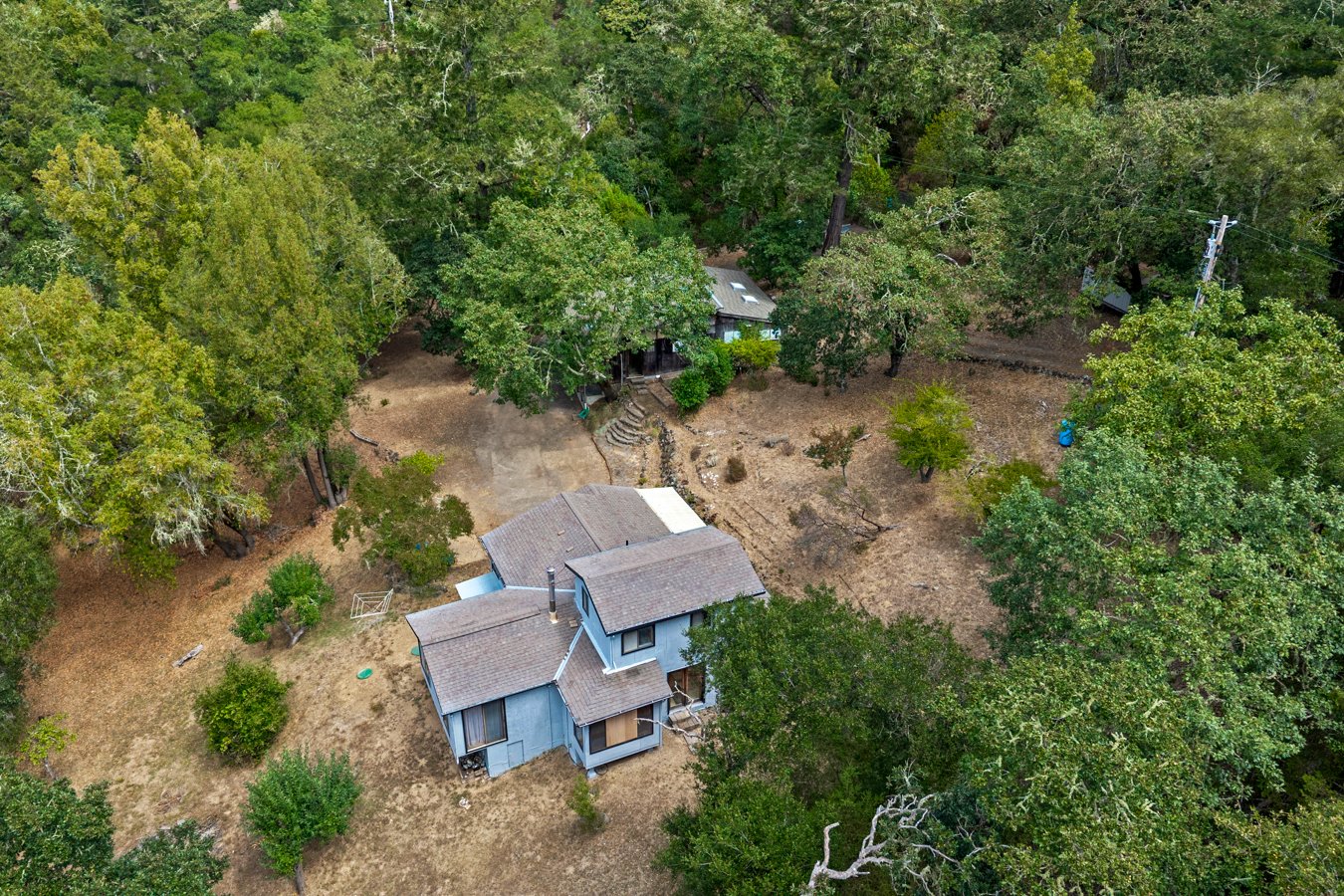 Aerial view of a residential property surrounded by trees, with a house, a backyard, and a driveway.