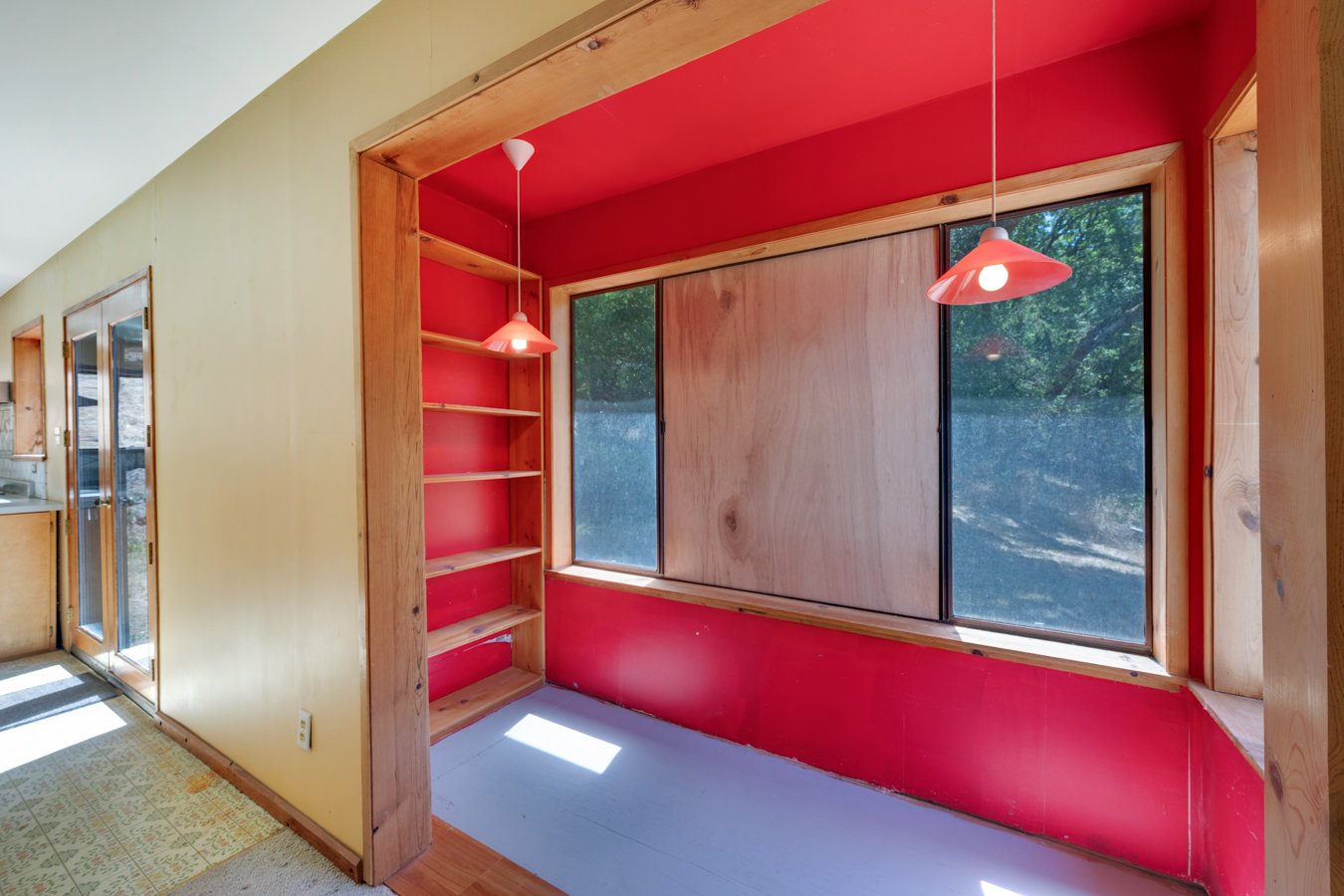 Empty nook with built-in shelves, large window, red interior walls, and hanging pendant lights in a house.