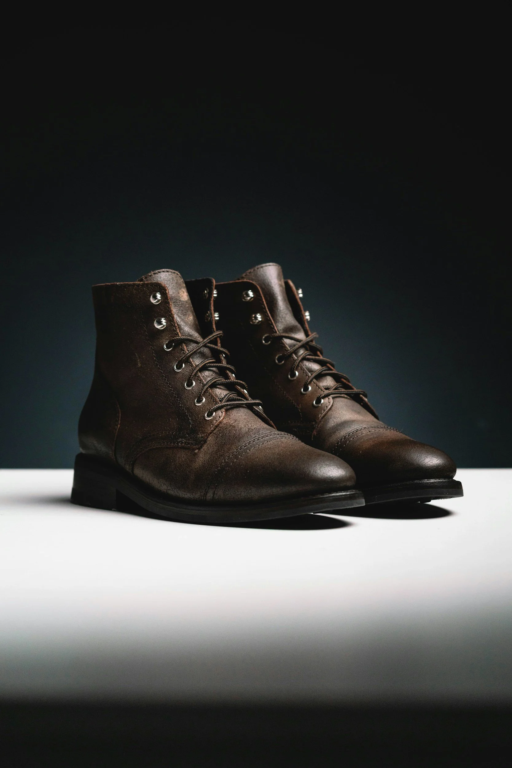 A pair of brown leather lace-up boots on a white surface against a dark background.