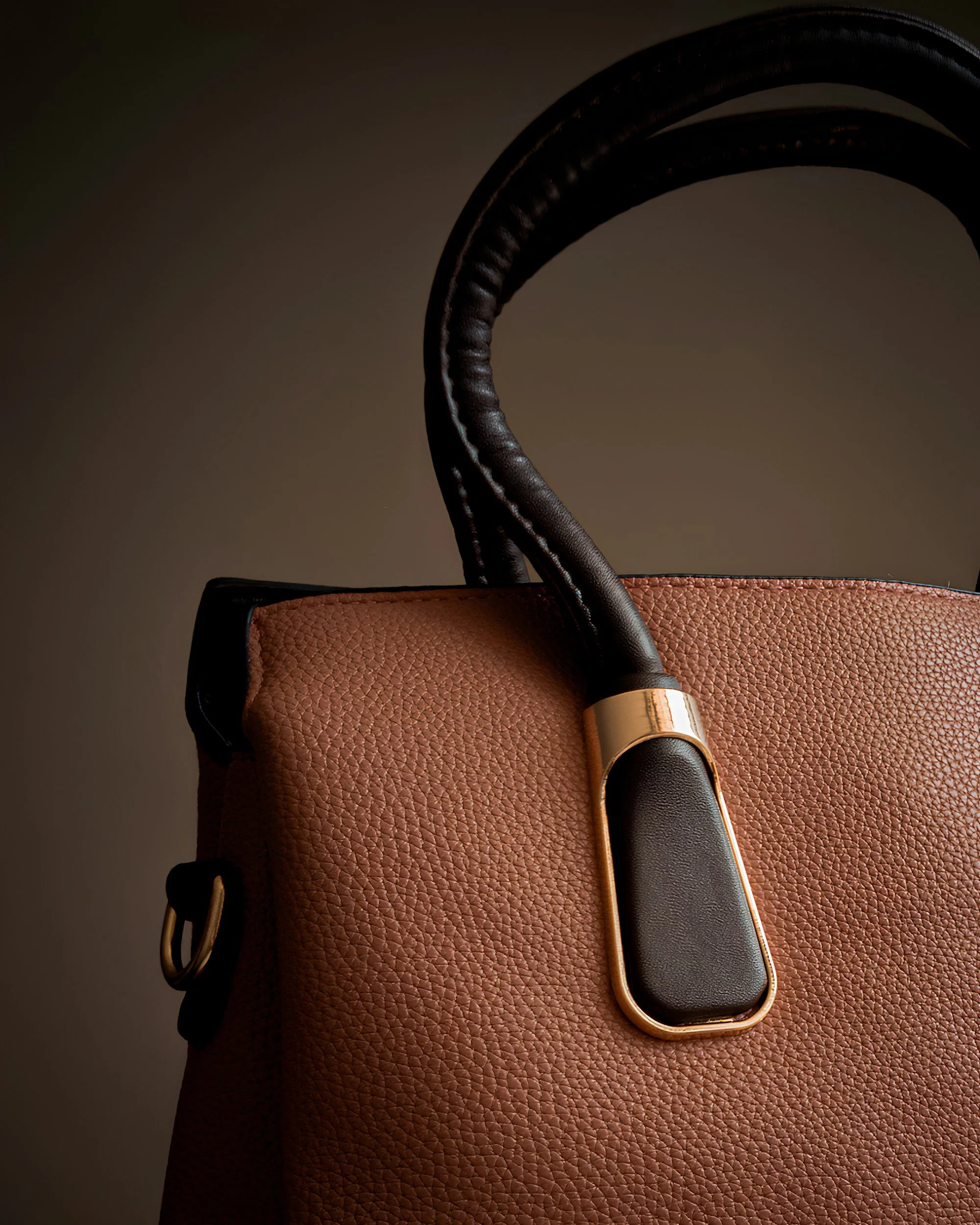 Close-up of a leather handbag with a black handle and gold hardware detail.