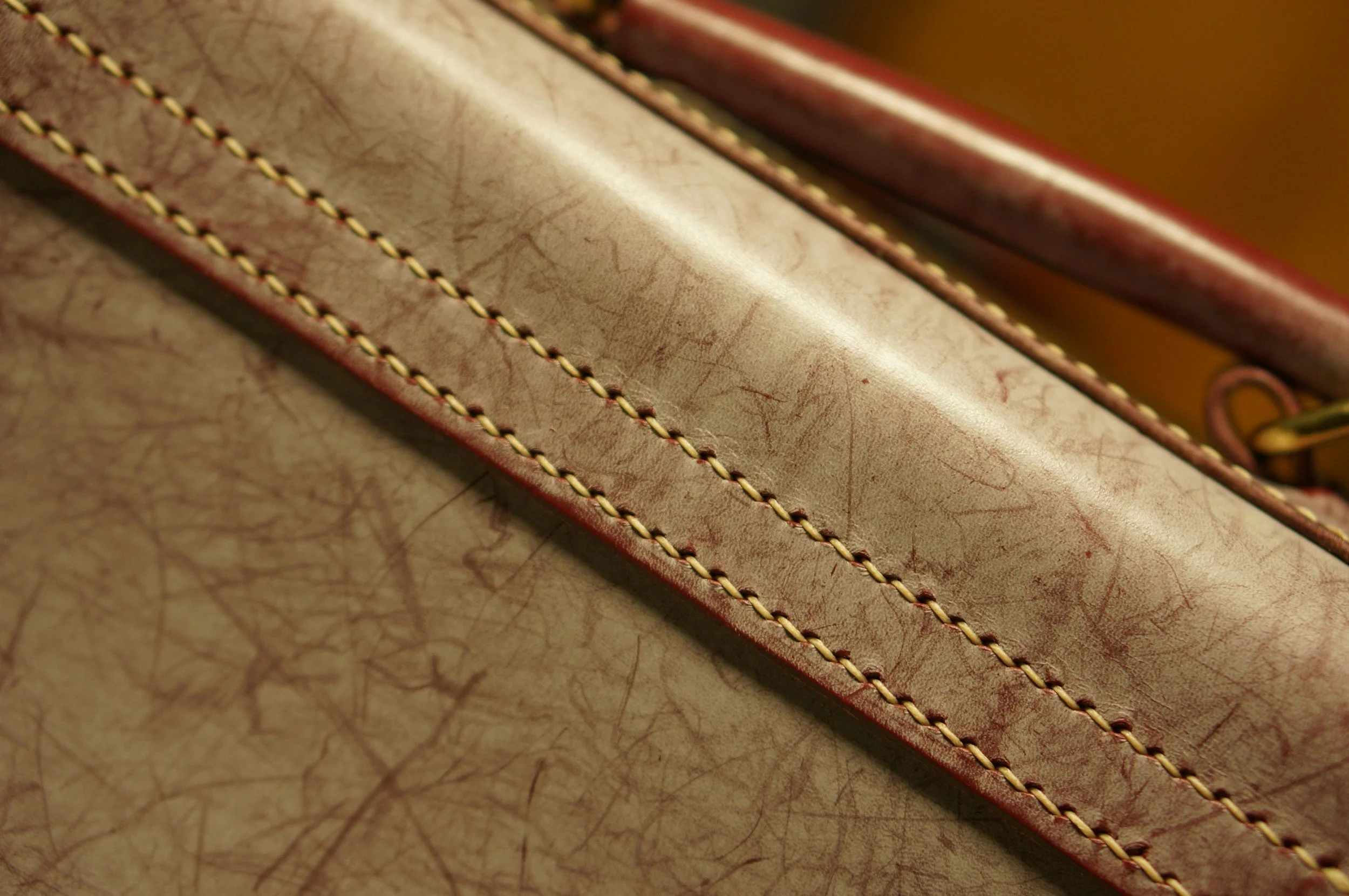 Close-up image of two leather straps with detailed stitching on a textured leather surface.
