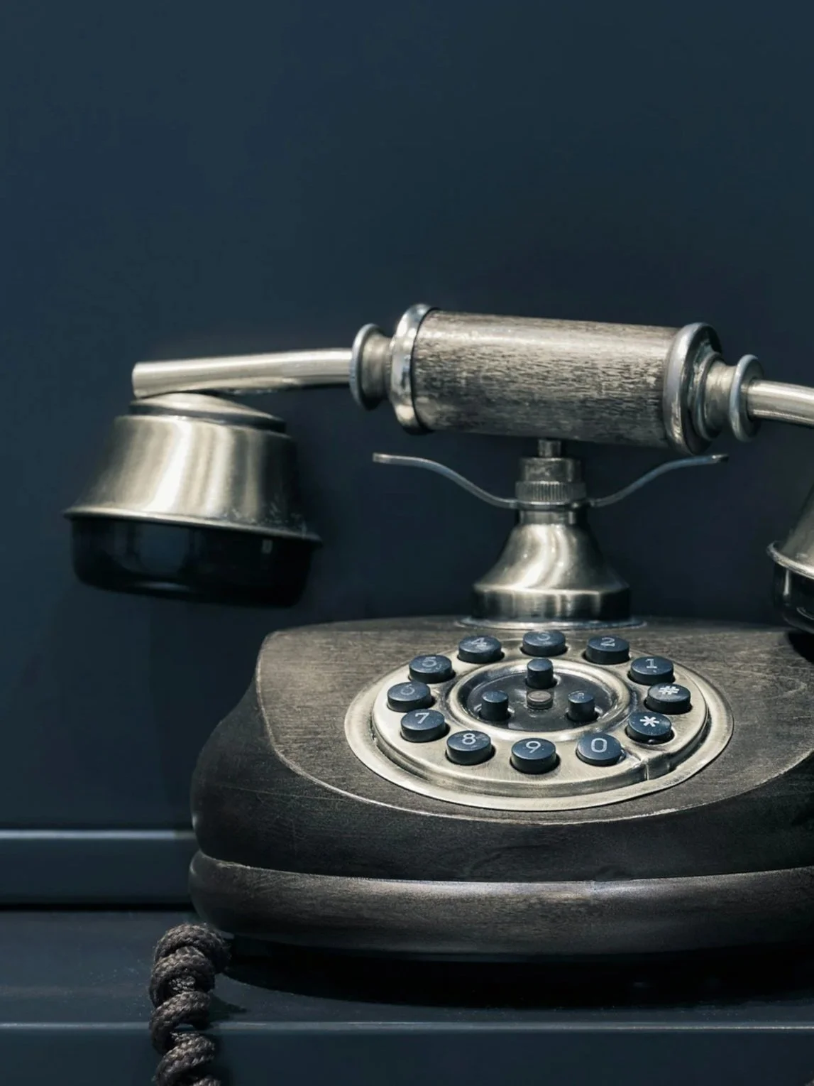 Vintage rotary telephone with a dark wooden base and metallic components, placed against a dark background.